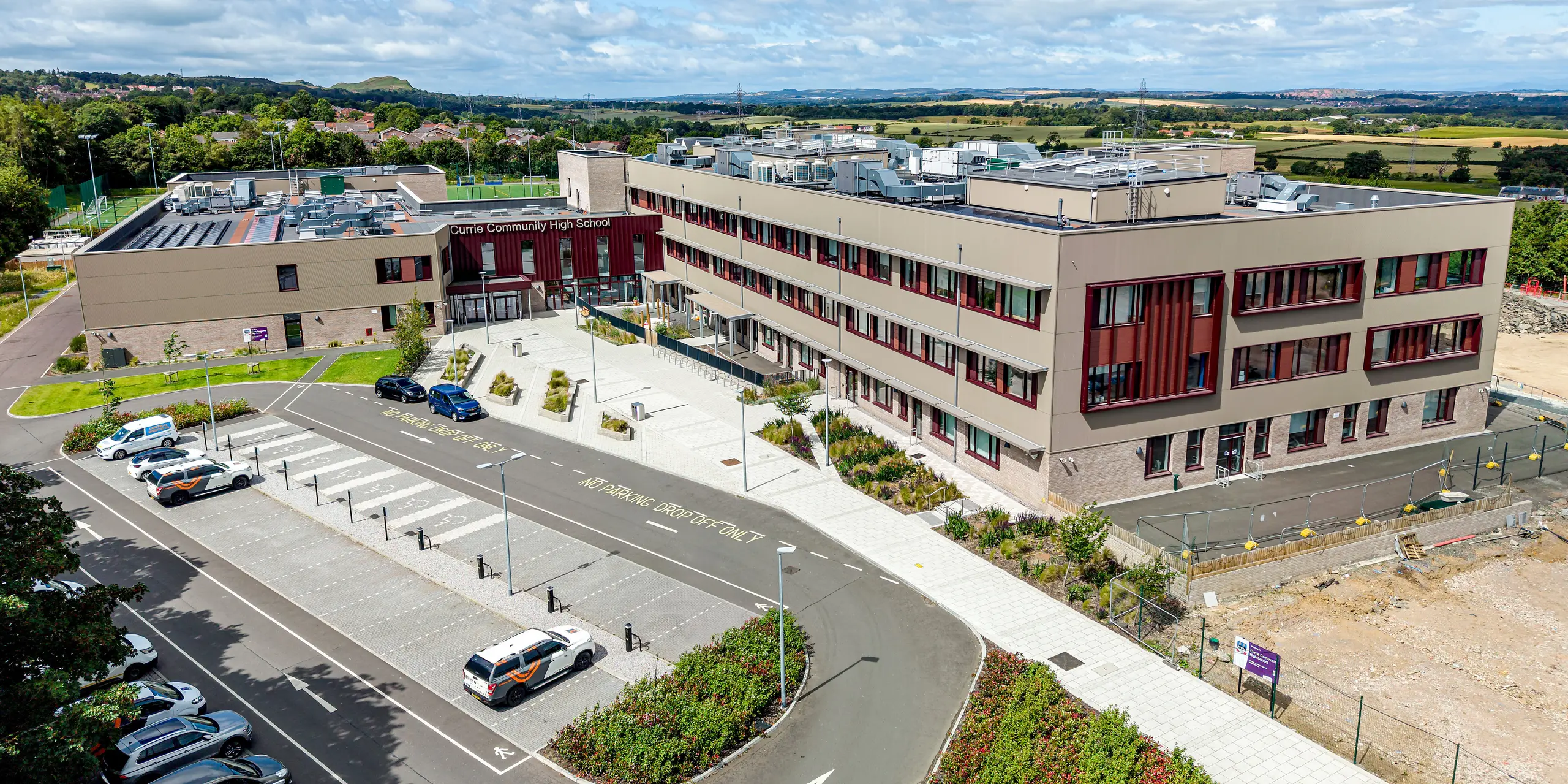 La vue aérienne du lycée Currie Community High School d'Édimbourg met parfaitement en valeur la façade moderne en aluminium PREFA. Le profilé triangle en P.10 bronze Prefa confère aux volumes imposants du bâtiment une structure remarquable et une profondeur élégante. Les lignes verticales de la façade créent des jeux de lumière captivants, tandis que l'aluminium, durable et résistant à la corrosion, séduit par sa facilité d'entretien et son style architectural intemporel.