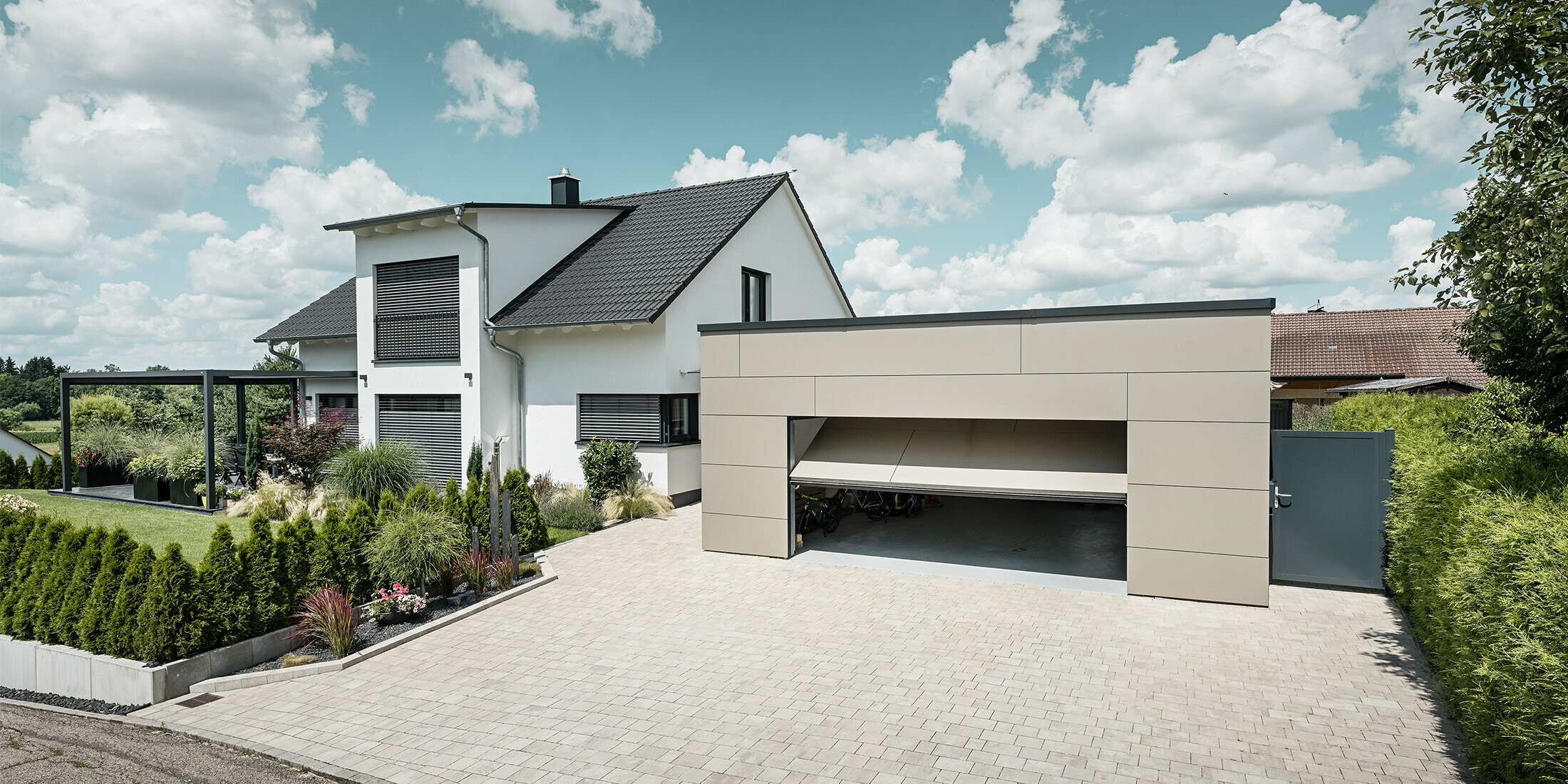 Die Fassade der Garage des Einfamilienhauses wurde komplett mit der PREFABOND Aluminium Verbundplatte in Bronze verkleidet. Das Garagentor ist geöffnet, davor ist eine große Einfahrt für mindestens 2 Autos gepflastert. 