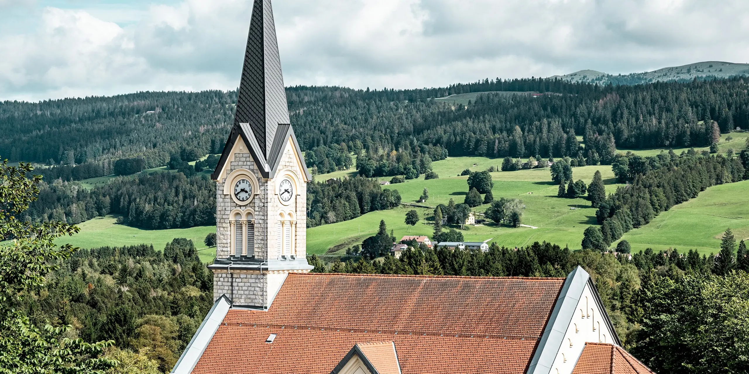 L'église du Sentier se dresse face au paysage vallonné impressionnant du Jura. Sa flèche élancée, revêtue de losanges PREFA 29 x 29 couleur Gris sombre P.10, crée un accent architectural saisissant. Cette toiture en aluminium de haute qualité est idéale pour les toits pentus, offrant durabilité, résistance aux intempéries et une esthétique soignée qui s'intègre harmonieusement au bâti historique.