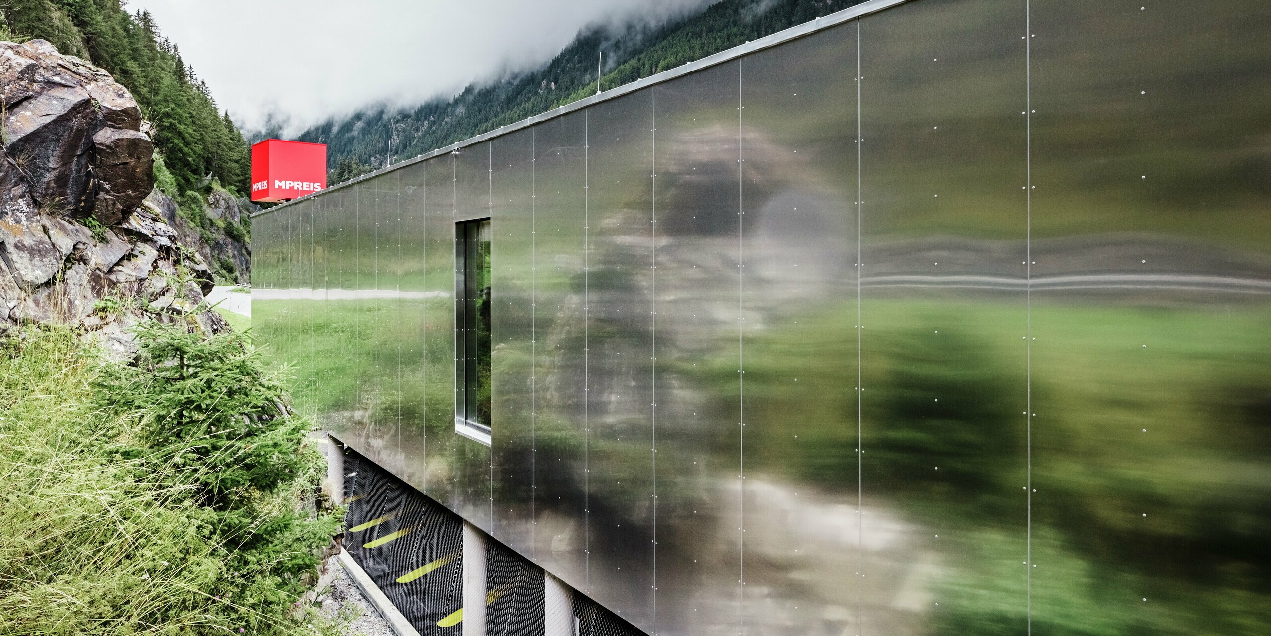 Gros plan de la façade en miroir du supermarché MPREIS à Sölden, au Tyrol. Les panneaux composites en aluminium de couleur spéciale Reflective Natural reflètent le paysage environnant des Alpes de l'Ötztal. Les panneaux installés sans joint créent une surface mate et brillante qui permet à l'architecture moderne de fusionner avec la nature.