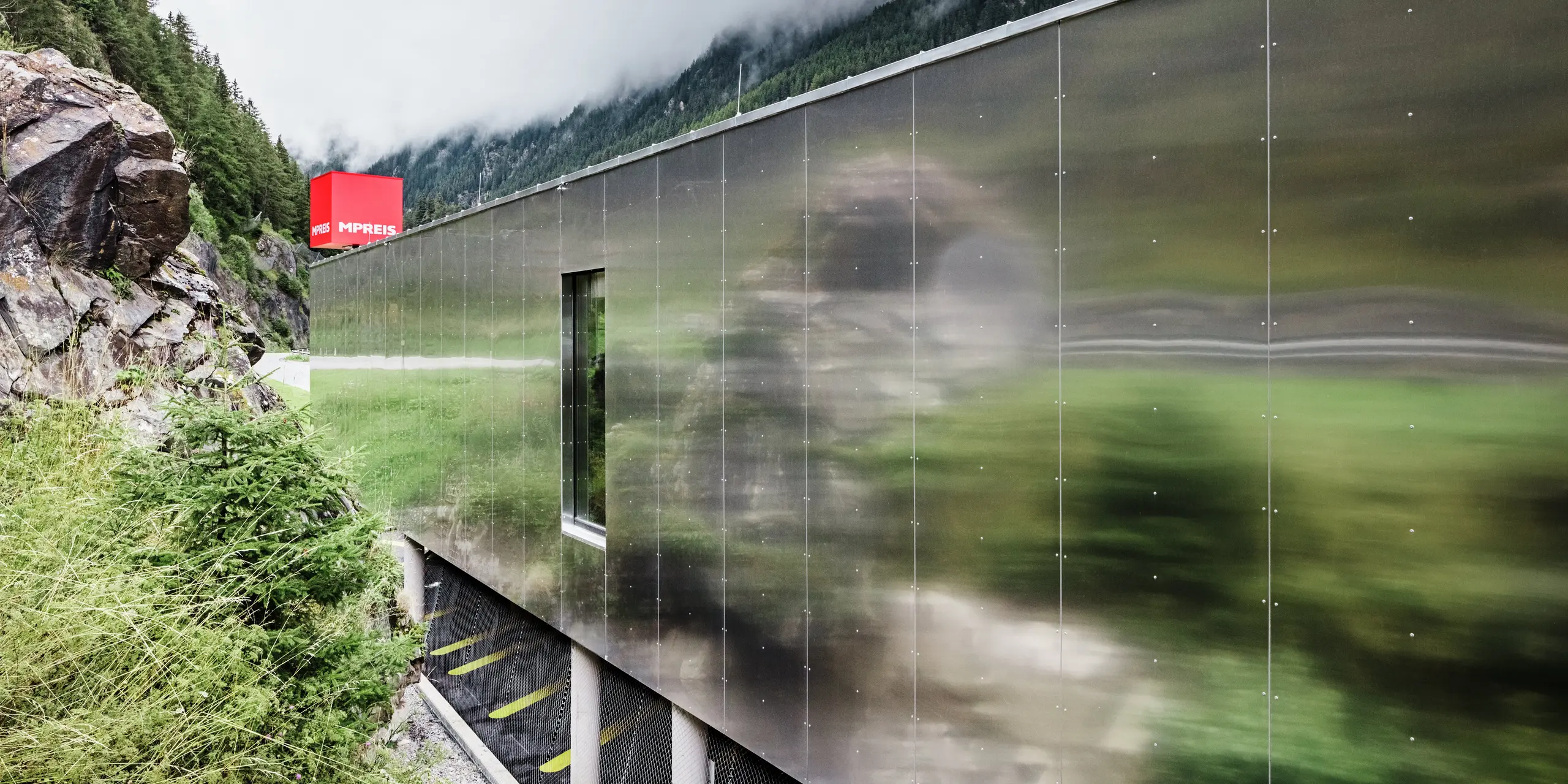 Gros plan de la façade en miroir du supermarché MPREIS à Sölden, au Tyrol. Les panneaux composites en aluminium de couleur spéciale Reflective Natural reflètent le paysage environnant des Alpes de l'Ötztal. Les panneaux installés sans joint créent une surface mate et brillante qui permet à l'architecture moderne de fusionner avec la nature.