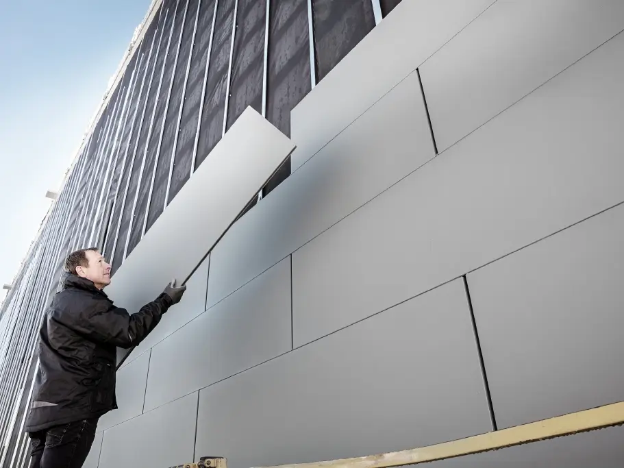 Photos d'une façade partiellement achevée, habillée avec des Siding PREFA en largeur 500. Le couvreur installe un autre panneau de façade. La vue a été prise d'en bas. 