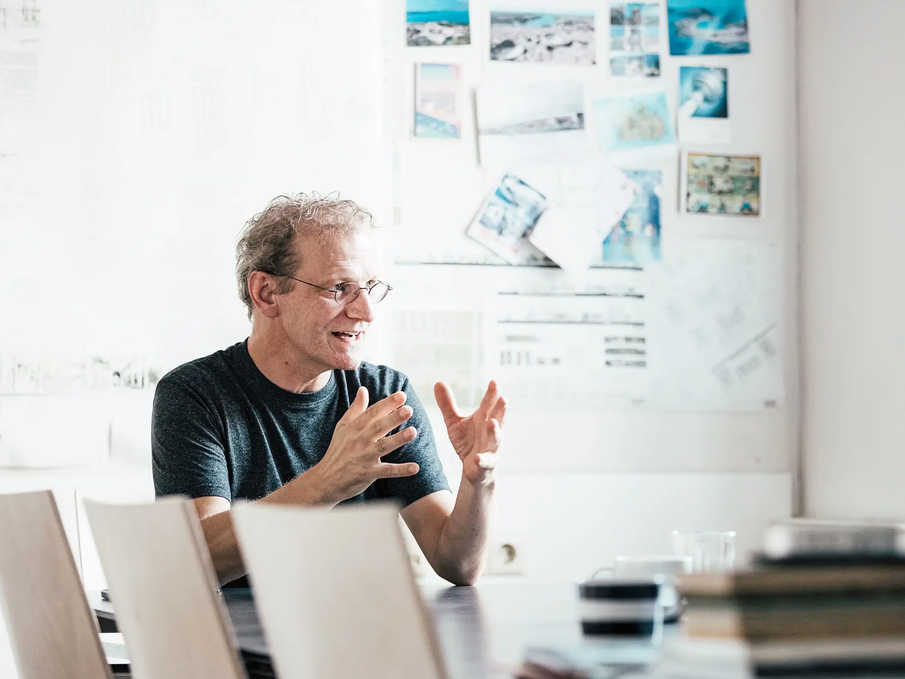 Portrait d'Anton Mariacher dans son bureau lumineux aménagé dans un bâtiment ancien. Sur les murs du couloir, des feuilles, des photos encadrées et des plans.