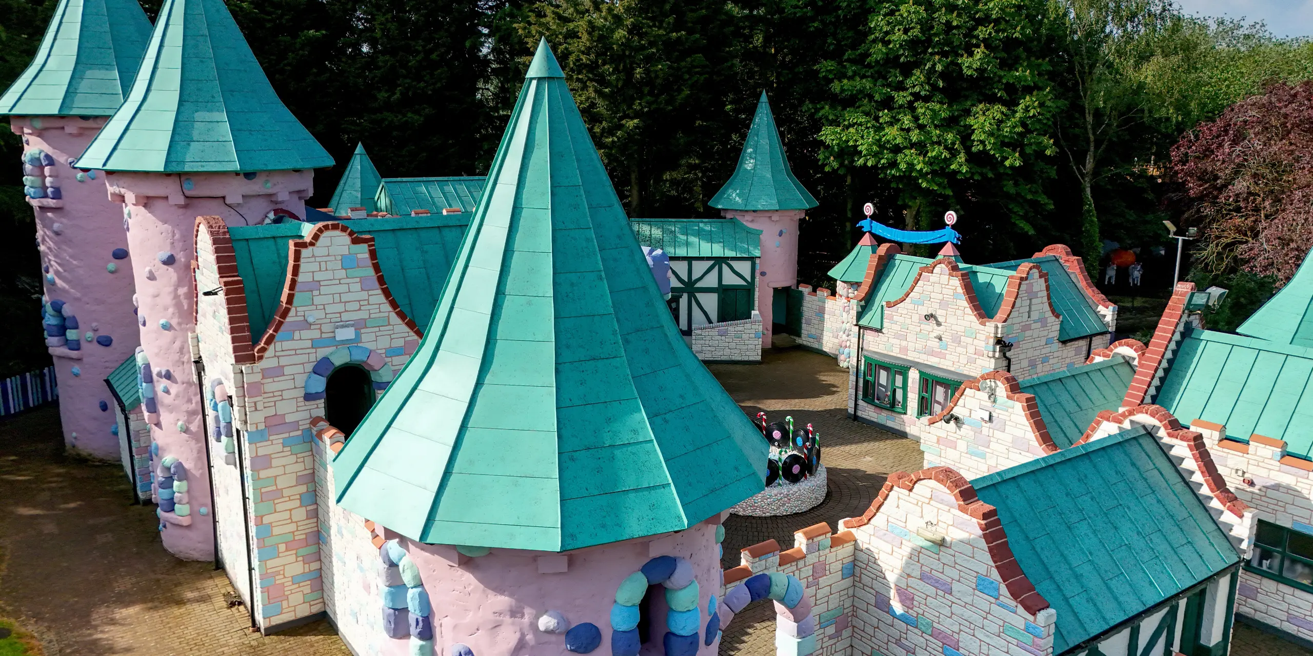 Vue détaillée d'un paysage de château féerique à Sundown Adventureland, avec ses tours coniques imposantes qui attirent le regard. Les toitures en aluminium PREFALZ, couleur P.10 vert de gris, définissent l'aspect général, soulignant avec élégance les formes courbes et les géométries complexes du toit. Des joints debout précis témoignent d'une qualité d'exécution irréprochable. Par ailleurs, les toitures PREFA impressionnent par leur extrême durabilité, leur résistance à la corrosion et leur fiabilité face à des conditions climatiques variées.