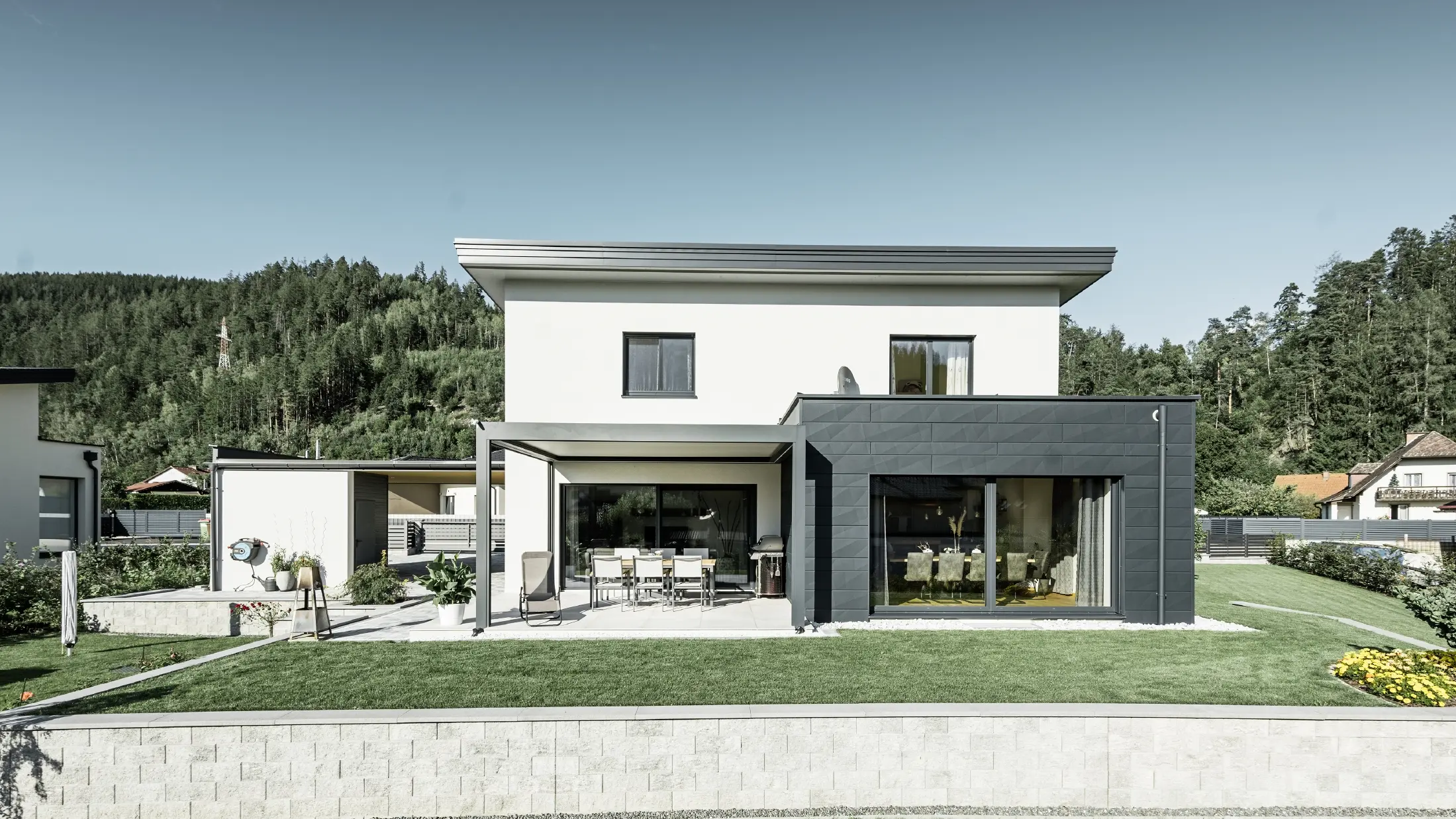 Neu gebautes Einfamilienhaus mit Zubau; Anbau hebt sich optisch vom Rest des Hauses ab, da er mit dem PREFA Fassadenpaneelen Siding.X in Anthrazit verkleidet ist. Der Rest der Fassade ist weiß verputzt.