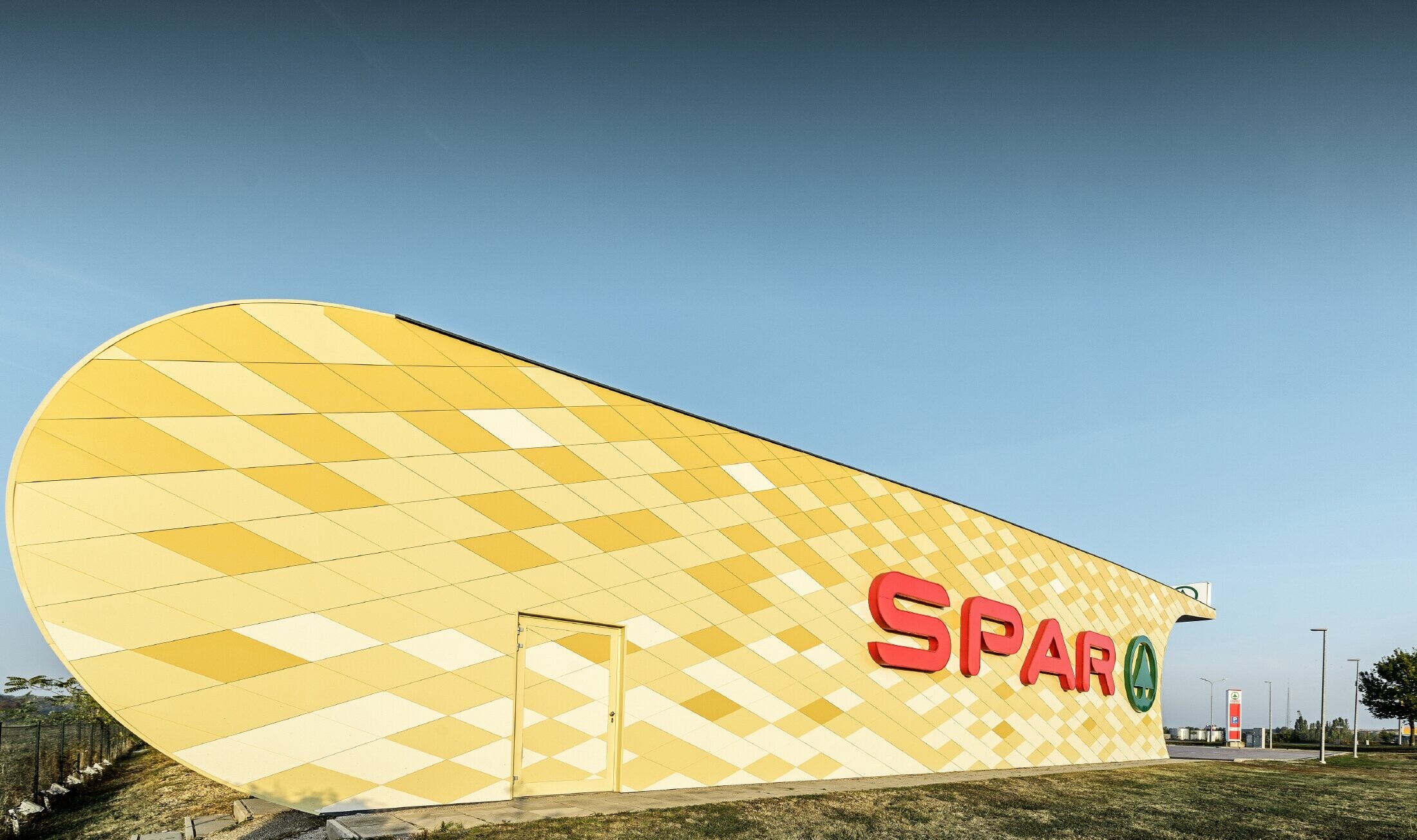 Magasin Spar — Façade en aluminium PREFA habillée de losanges jaune pâle à orange et arborant le logo Spar
