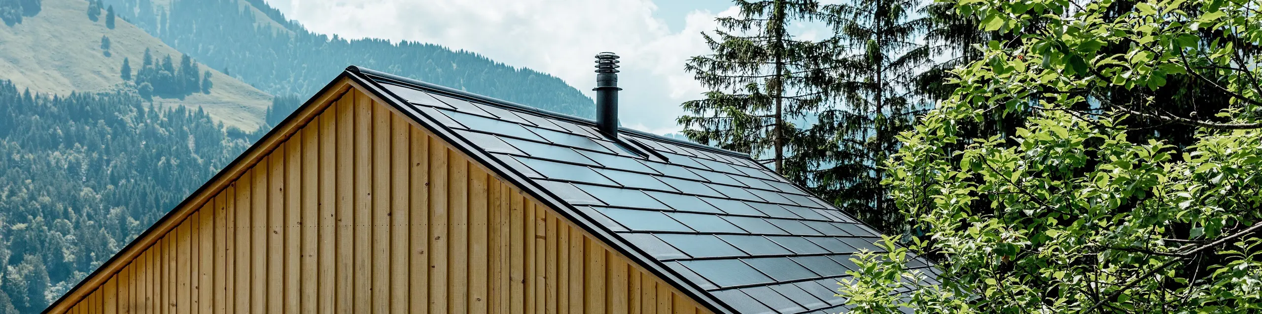 Entre les cimes verdoyantes des arbres et l’impressionnant paysage montagneux, la maison Immi se dévoile comme un refuge moderne au cœur d’Ebnit, dans les Alpes. La façade en sapin blanc naturel s’associe à une élégante toiture solaire PREFA en P.10 Noir. Les tuiles solaires intégrées et les R.16 conjuguent production d’énergie durable, protection robuste contre les intempéries et architecture épurée, harmonieusement intégrée au paysage et répondant aux exigences les plus élevées.