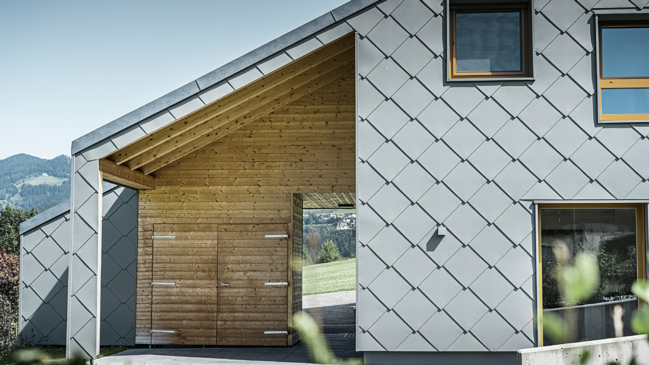 L’entrée couverte est faite de boiseries horizontales ; le reste de la façade est revêtu du losange de façade grand format PREFA en aluminium gris souris