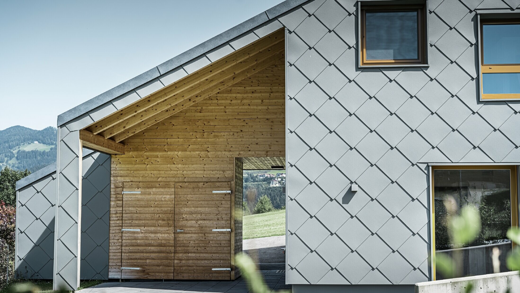 L’entrée couverte est faite de boiseries horizontales ; le reste de la façade est revêtu du losange de façade grand format PREFA en aluminium gris souris