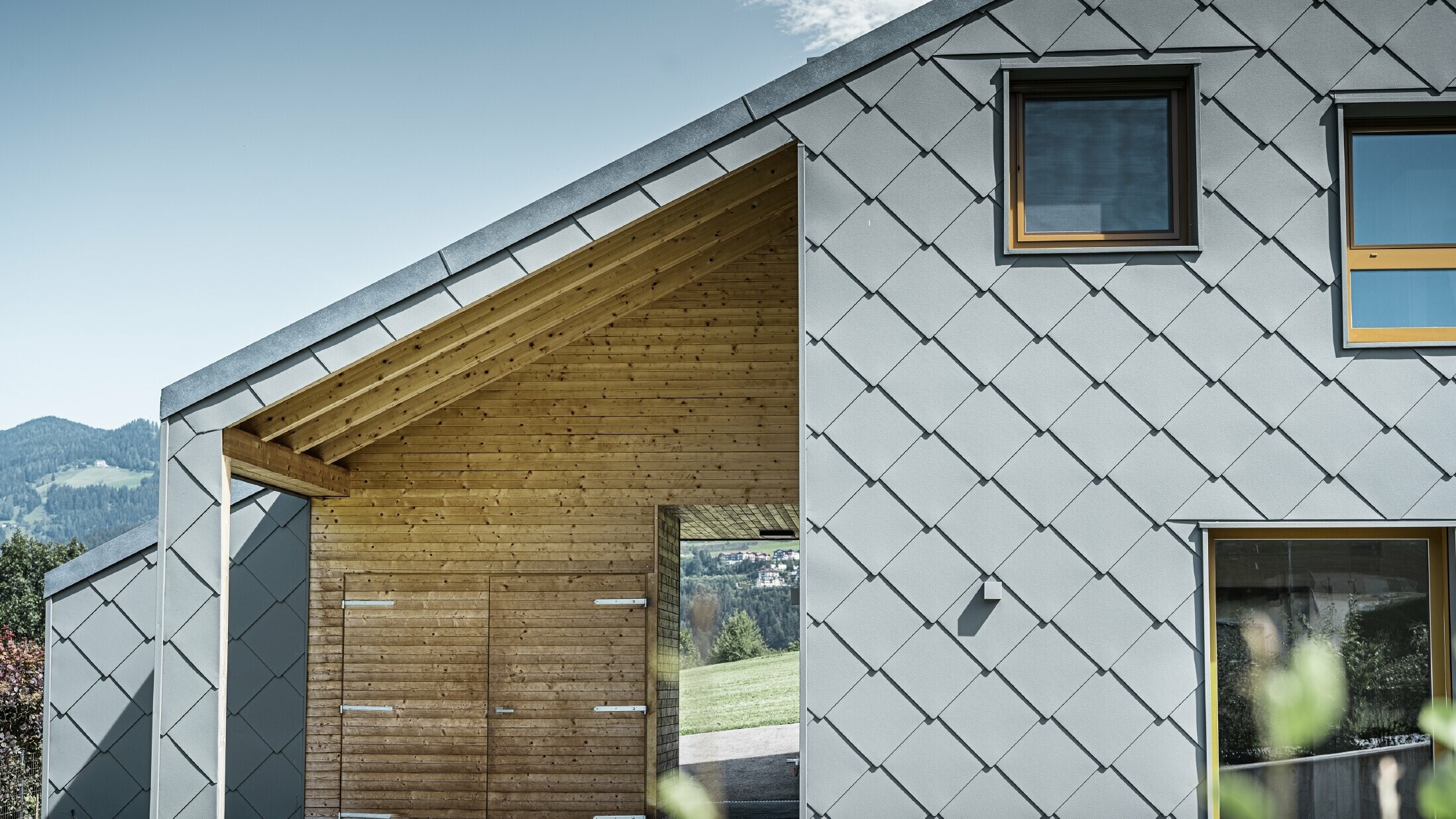 L’entrée couverte est faite de boiseries horizontales ; le reste de la façade est revêtu du losange de façade grand format PREFA en aluminium gris souris