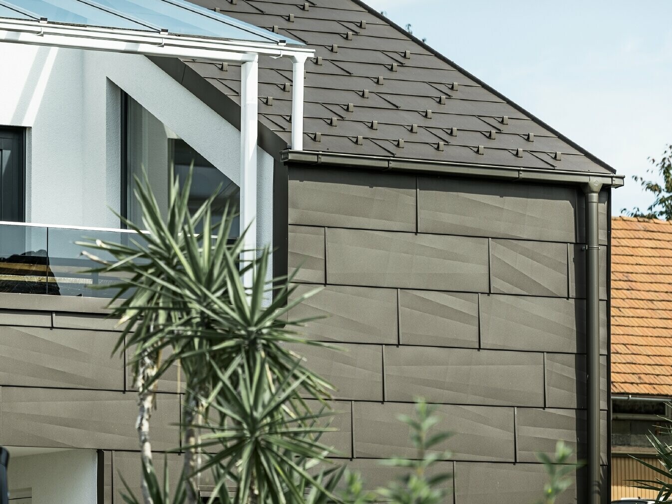 Extension avec terrasse de toit revêtue du système complet PREFA ; pour le toit et la façade, le choix s'est porté sur le panneau de toiture et de façade FX.12 PREFA. Pour l'écoulement des eaux de pluie, le choix s'est également porté sur la gouttière carrée PREFA avec tuyau de descente PREFA et accessoires complets en brun.
