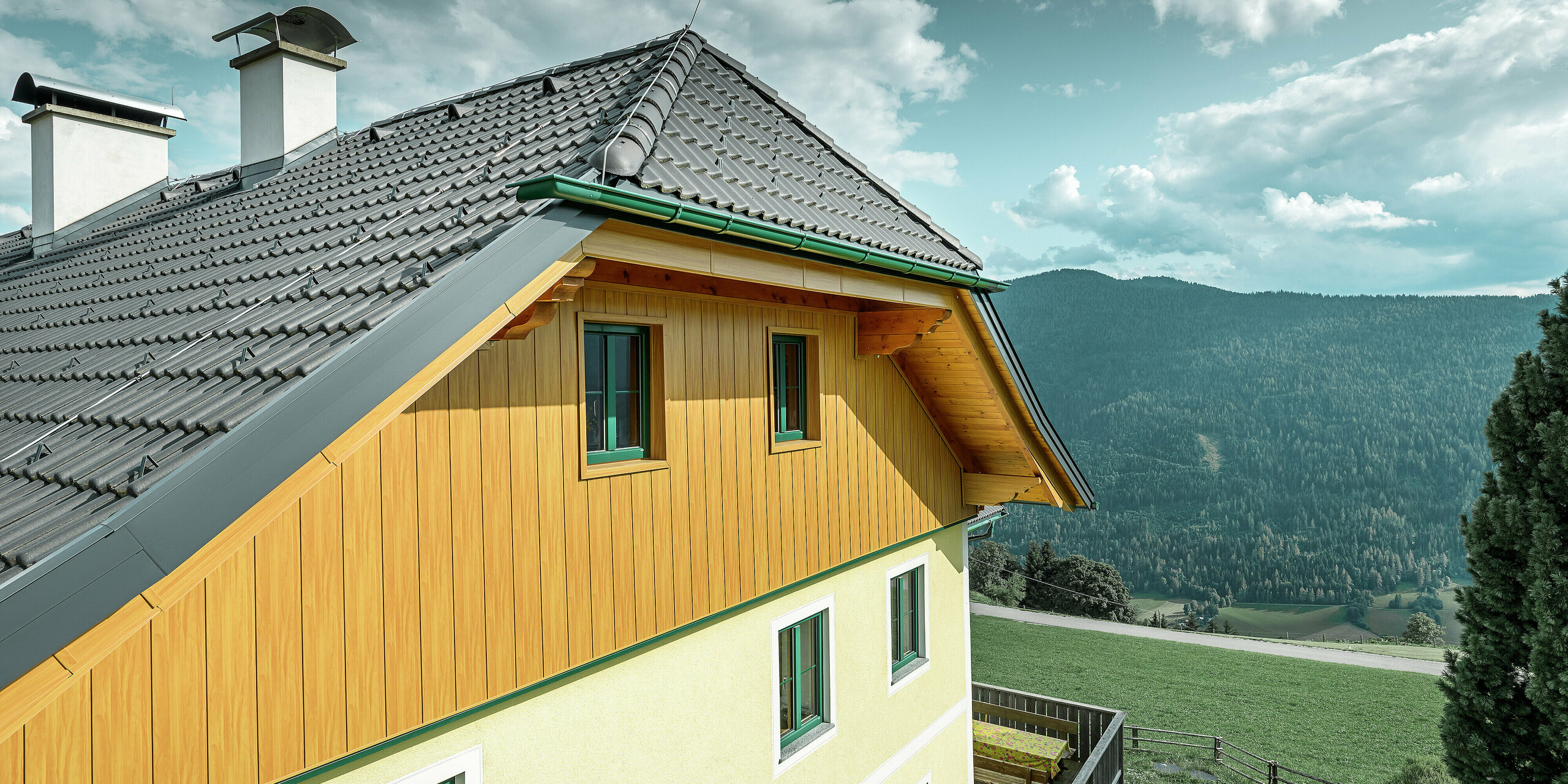 Detailansicht der Giebelverkleidung mit PREFA Sidings in Eiche natur an einem Wohnhaus in Ranten mit Blick auf die umliegende Berglandschaft.