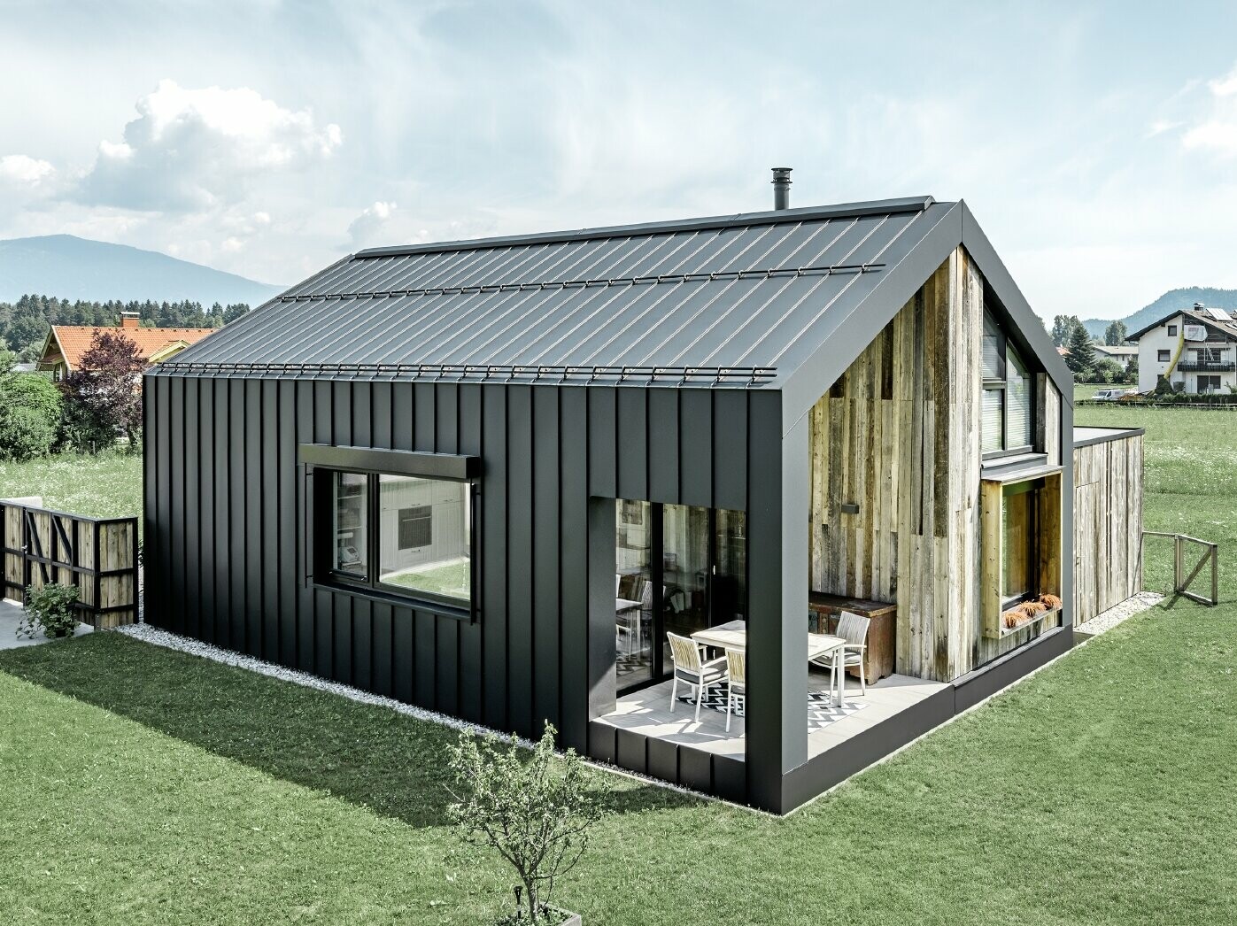 Maison individuelle avec toit à pignon ; la toiture et la façade sont recouvertes avec PREFALZ de PREFA en P.10 anthracite. Les bacs de la surface de toit se prolongent jusque sur la façade. Une partie de la façade est revêtue de bois patiné.