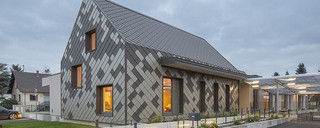 Vue de face du périscolaire revêtu de losange de toiture et de façade PREFA dans la teinte brun et bronze au crépuscule.