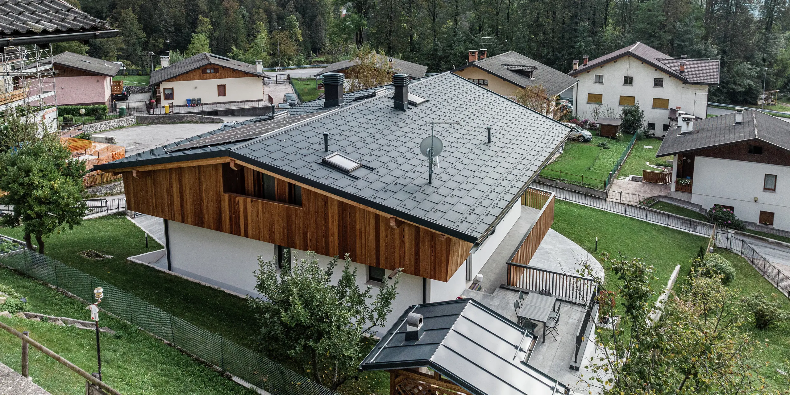 Maison familiale rénovée à Agordo, en Italie, avec un toit en aluminium durable. Le PREFA R.16 en P.10 anthracite offre une protection optimale contre les intempéries et s'intègre harmonieusement dans l'environnement. Le système de gouttière PREFA avec gouttière et tuyau de descente assure un drainage efficace de l'eau. La combinaison d'une façade en bois naturel à l'étage supérieur, d'une façade en plâtre blanc au rez-de-chaussée et d'aluminium de haute qualité dans la zone du toit confère au bâtiment une apparence élégante et moderne.