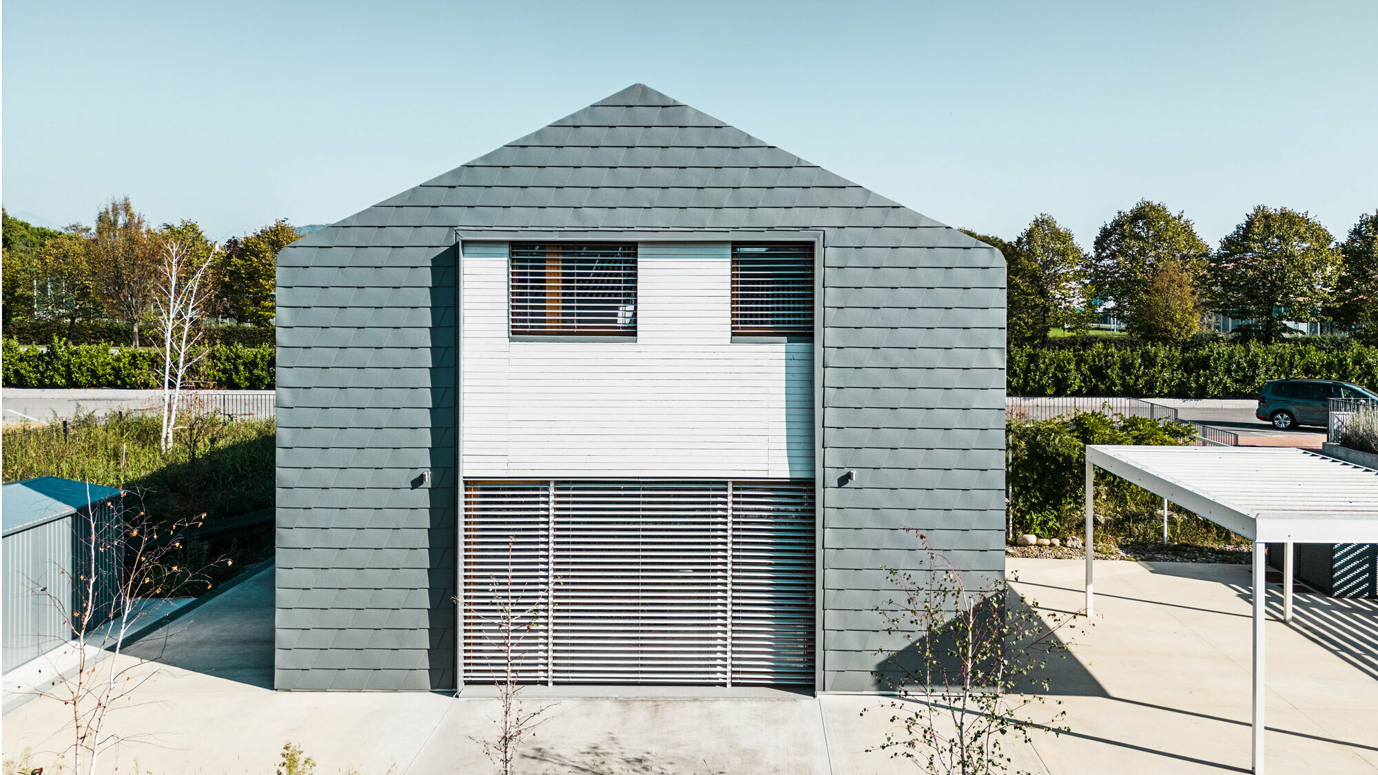 Vue de face de la maison, en direction du terrain. Une seconde rupture visuelle est visible sur la façade, toujours avec le lattage en bois blanc.