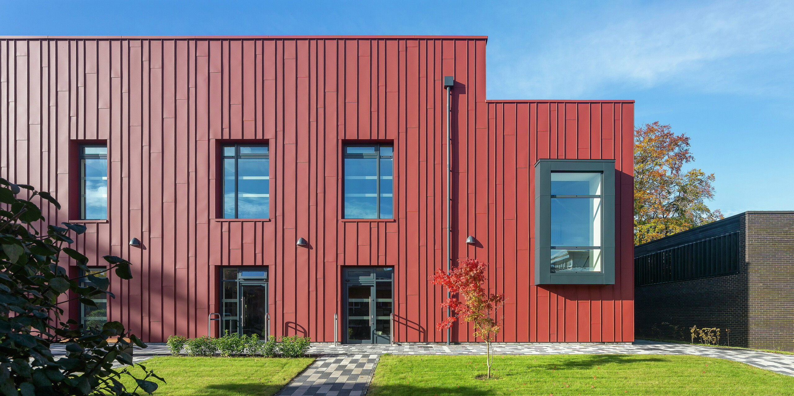 Architecture moderne avec PREFALZ : La façade du Soldiers' Centre de Pirbright impressionne par son élégant revêtement à joint debout en PREFALZ en P.10 rouge oxyde. Les cadres de fenêtres élégants en P.10 anthracite apportent des accents ciblés et confèrent au bâtiment une apparence dynamique. Durables, esthétiques et durables - les produits en aluminium PREFA pour des concepts de construction innovants.