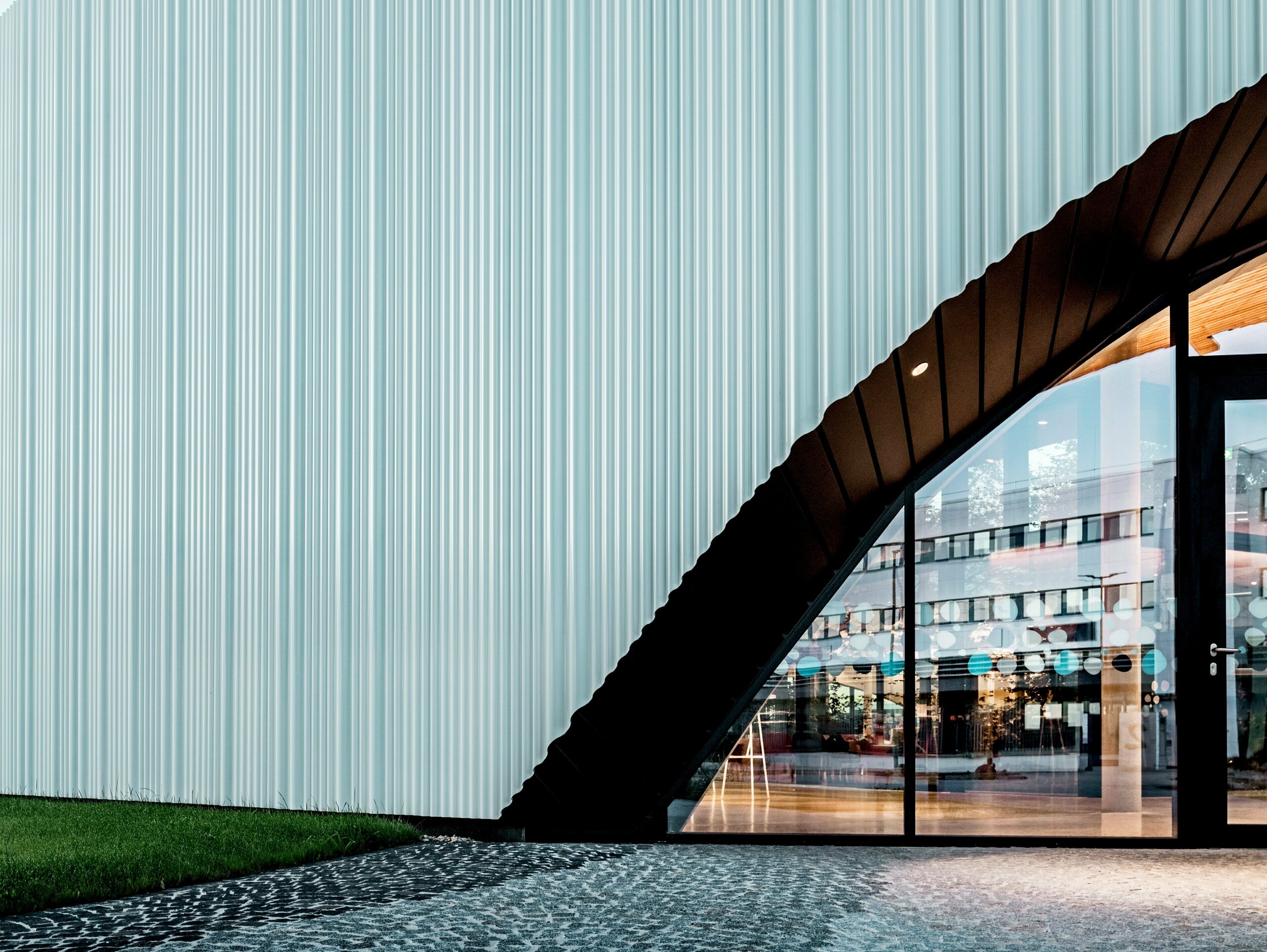 Une conception de façade spectaculaire avec le profil extrudé PREFA Sinus en aluminium de haute qualité habille le siège de l’entreprise LKW Walter à Vienne. La structure profilée, légèrement ondulée et disposée verticalement, crée un élégant effet de vagues générant de fascinants jeux de lumière. Alors que le bâtiment moderne séduit par son langage formel épuré, la découpe courbe de la façade apporte un contraste architectural fort et distinctif. Les profils en aluminium, durables et résistants à la corrosion, dotés d’une fixation invisible, garantissent une enveloppe extérieure haut de gamme et sans entretien.