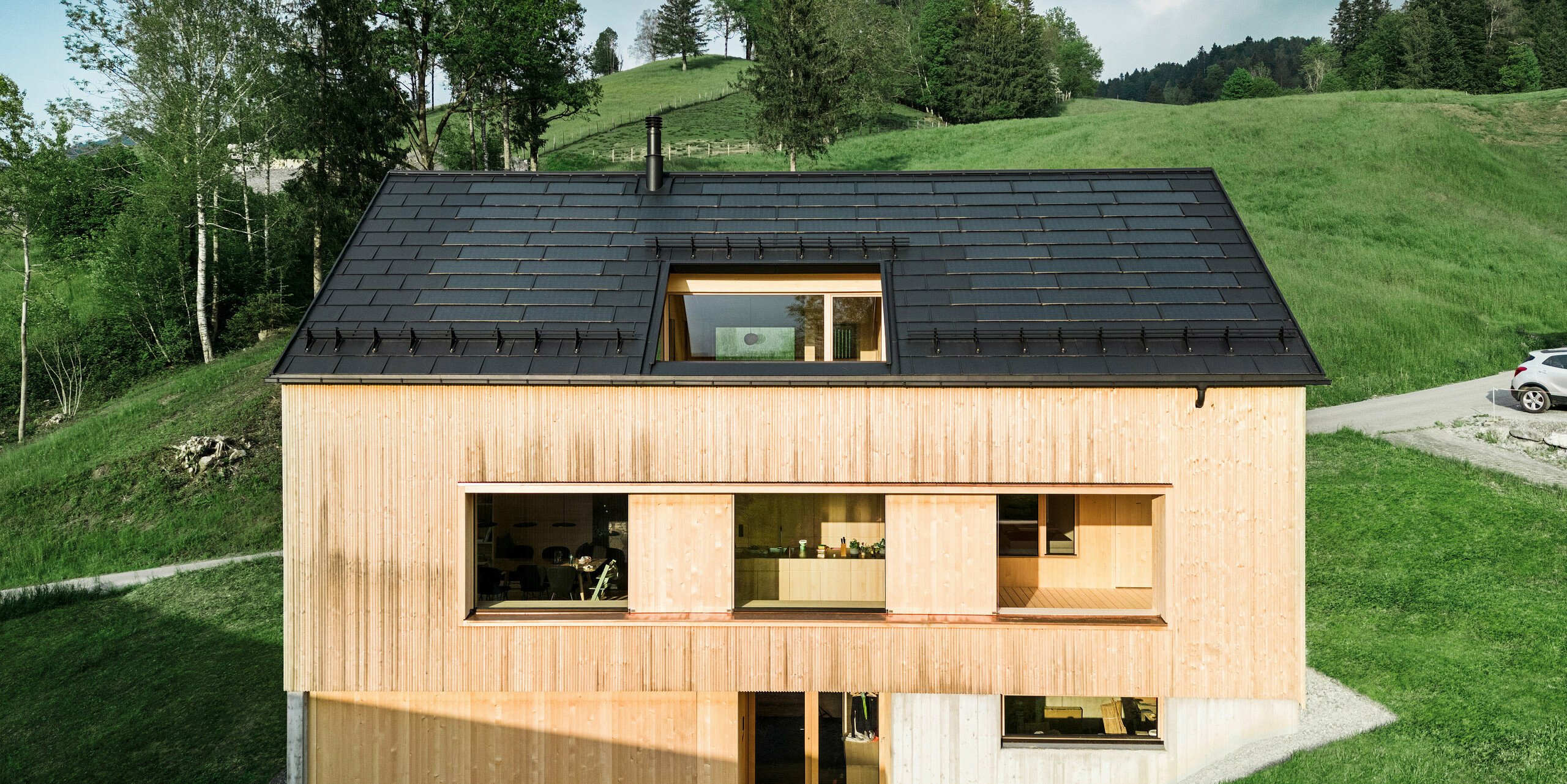 Maison individuelle dans la ville autrichienne d'Egg avec le panneau de toit solaire PREFA et le panneau de toit R.16 en noir, combinés à une façade en bois