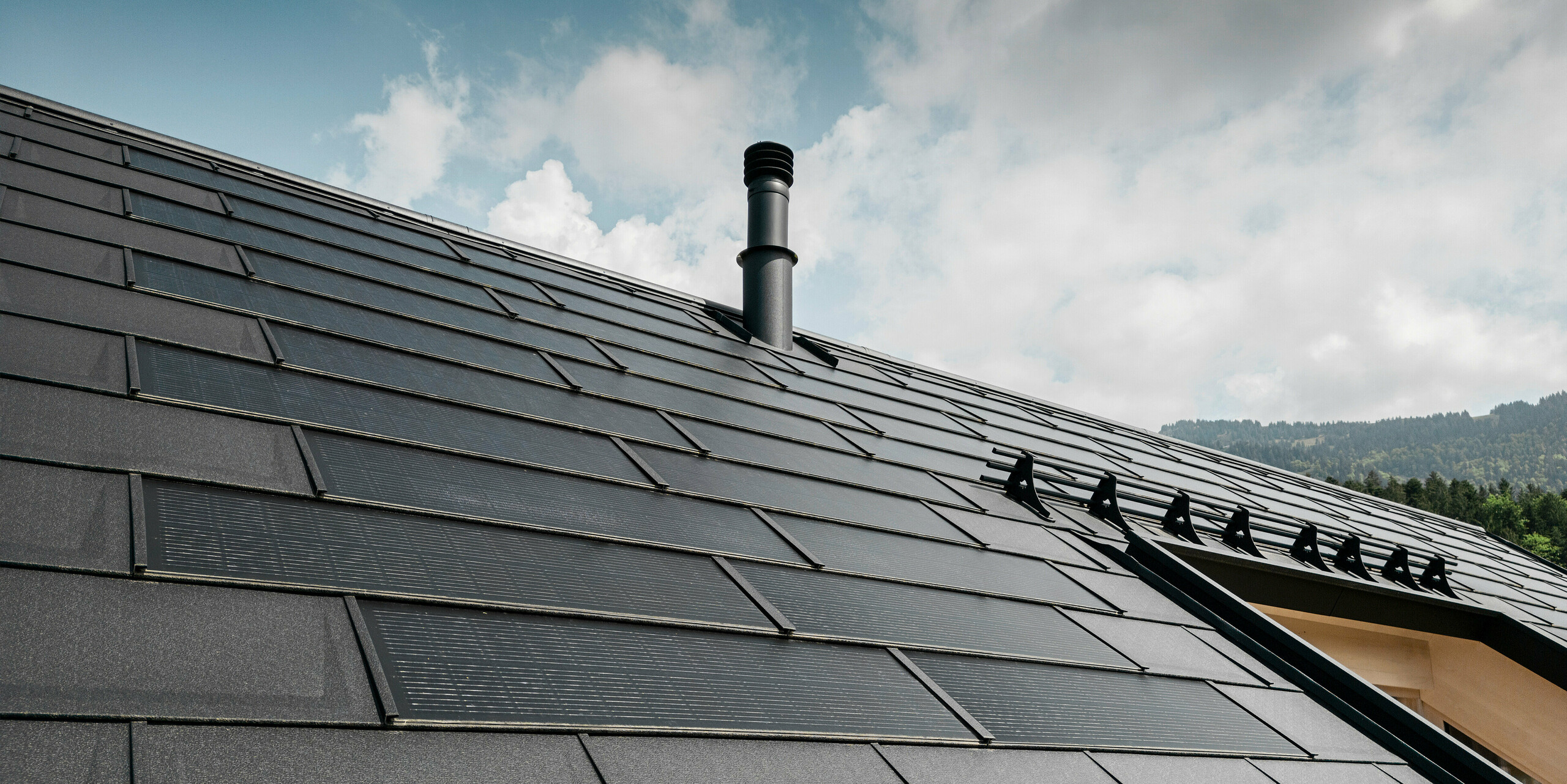 Maison individuelle dans la ville autrichienne d'Egg avec le panneau de toit solaire PREFA et le panneau de toit R.16 en noir, combinés à une façade en bois