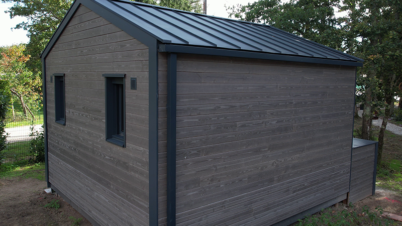 Vue latérale d'un lodge dont la couverture ainsi que les évacuations des eaux pluviales ont été sélectionnées en aluminium PREFA dans la teinte P.10 anthracite. 