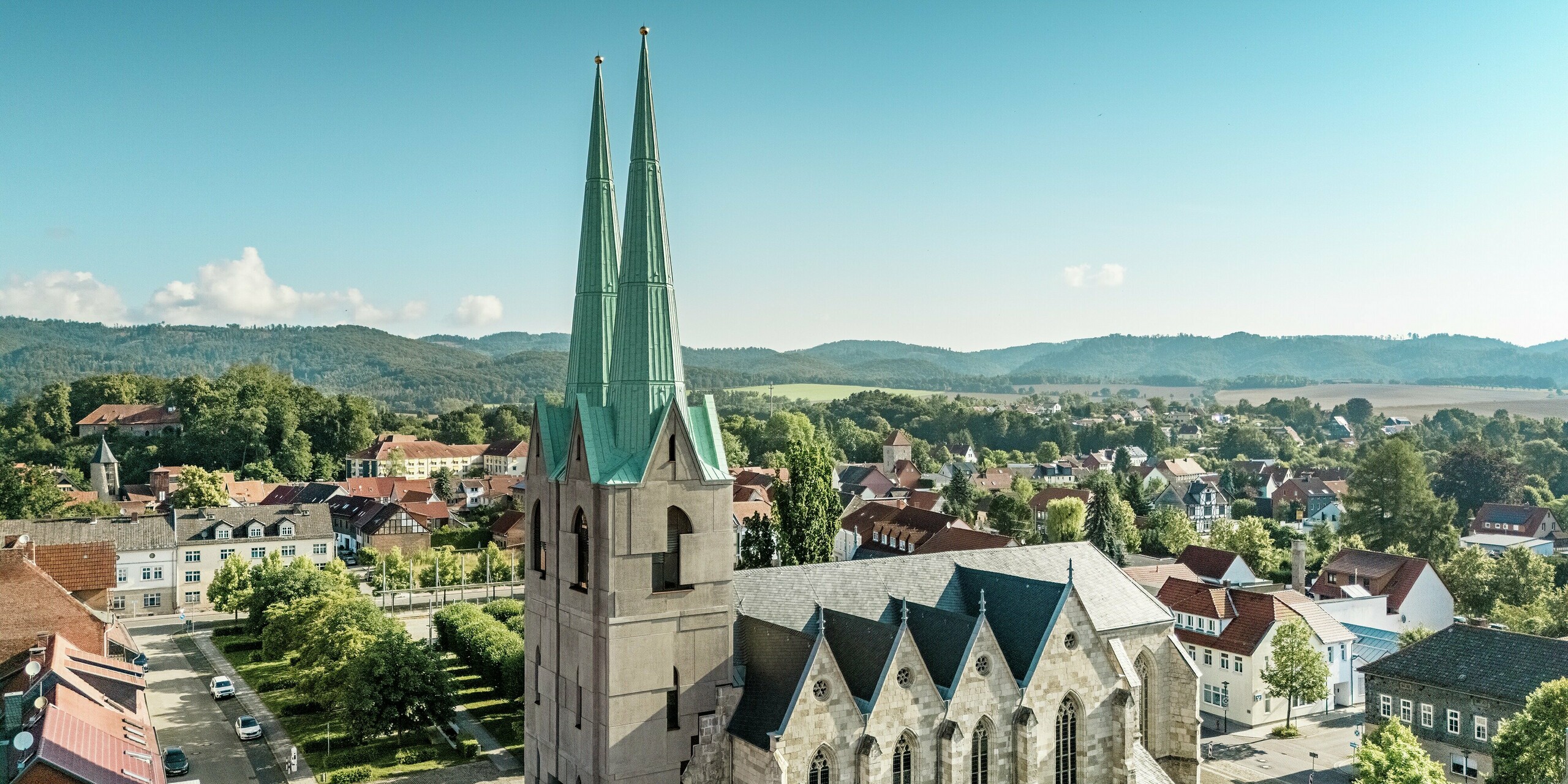 Vue aérienne du centre touristique rénové d'Ellrich, avec son architecture d'église remarquable. Les deux flèches élancées, revêtues de PREFALZ couleur P.10 Vert de gris, contrastent fortement avec le paysage urbain. La toiture en aluminium résistant aux intempéries allie esthétique historique et technologie moderne, et affirme avec force son engagement en faveur d'une architecture durable.
