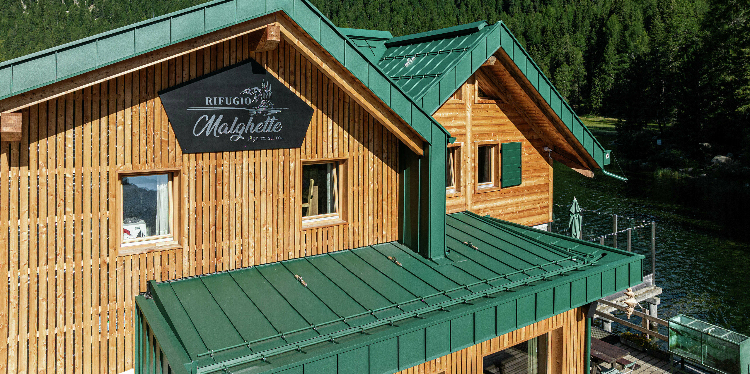 Vue détaillée des deux pignons du Rifugio Malghette. La façade en bois a été encadrée avec le joint debout PREFALZ sur le toit et la façade - durable, résistant aux tempêtes et parfait pour les conditions météorologiques extrêmes. Le revêtement en aluminium de haute qualité de couleur P.10 vert mousse s'intègre harmonieusement dans le paysage alpin et protège de manière fiable la cabane à une altitude de 1 888 m.