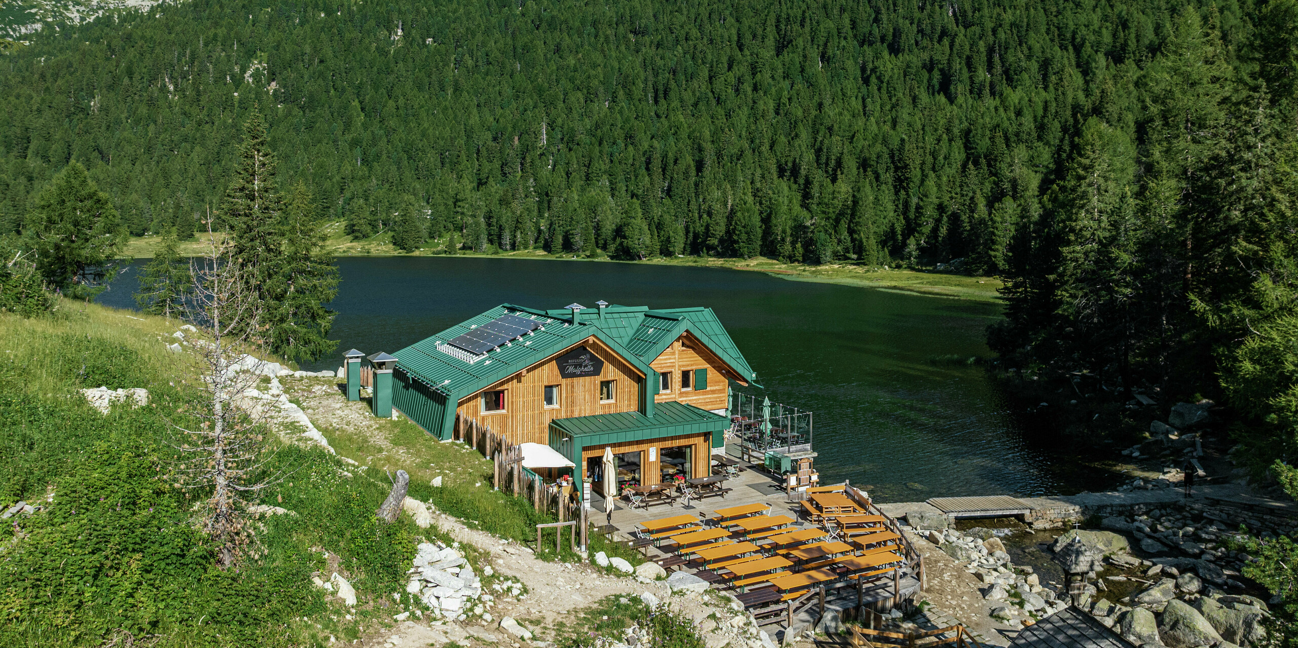 Le Rifugio Malghette à 1 888 m, idéalement situé au bord du lac, avec le toit PREFALZ en vert mousse P.10 - résistant aux intempéries, durable et parfaitement intégré dans la nature. La spacieuse terrasse ensoleillée invite les randonneurs à s'attarder et le toit en aluminium durable résiste même aux conditions météorologiques extrêmes en montagne.