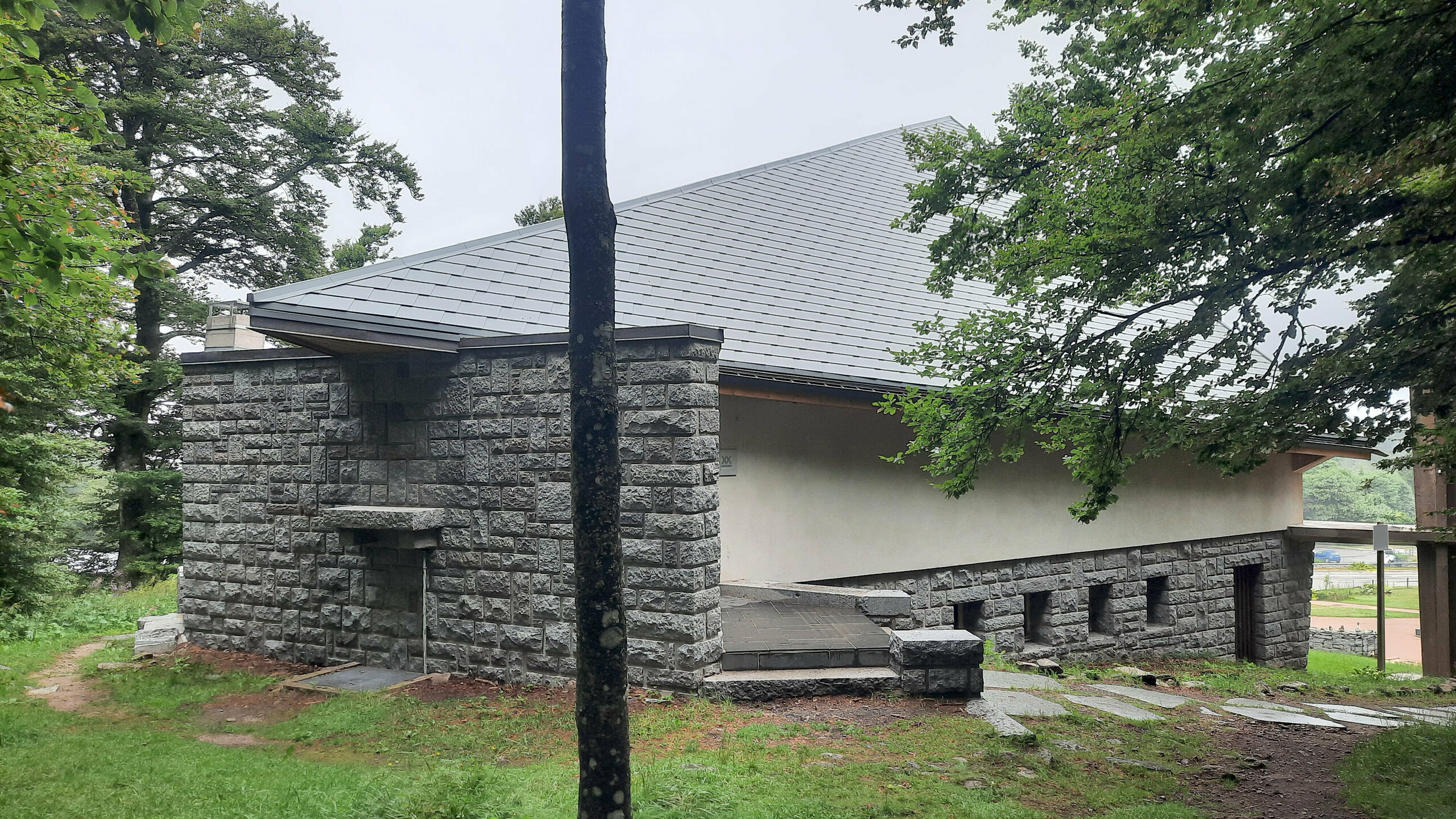 Photographie de l'arrière de la chapelle du col de la Schlucht, on aperçoit un mur en pierre de parement, une façade en crépi classique et un bout de la toiture en bardeaux en aluminium PREFA