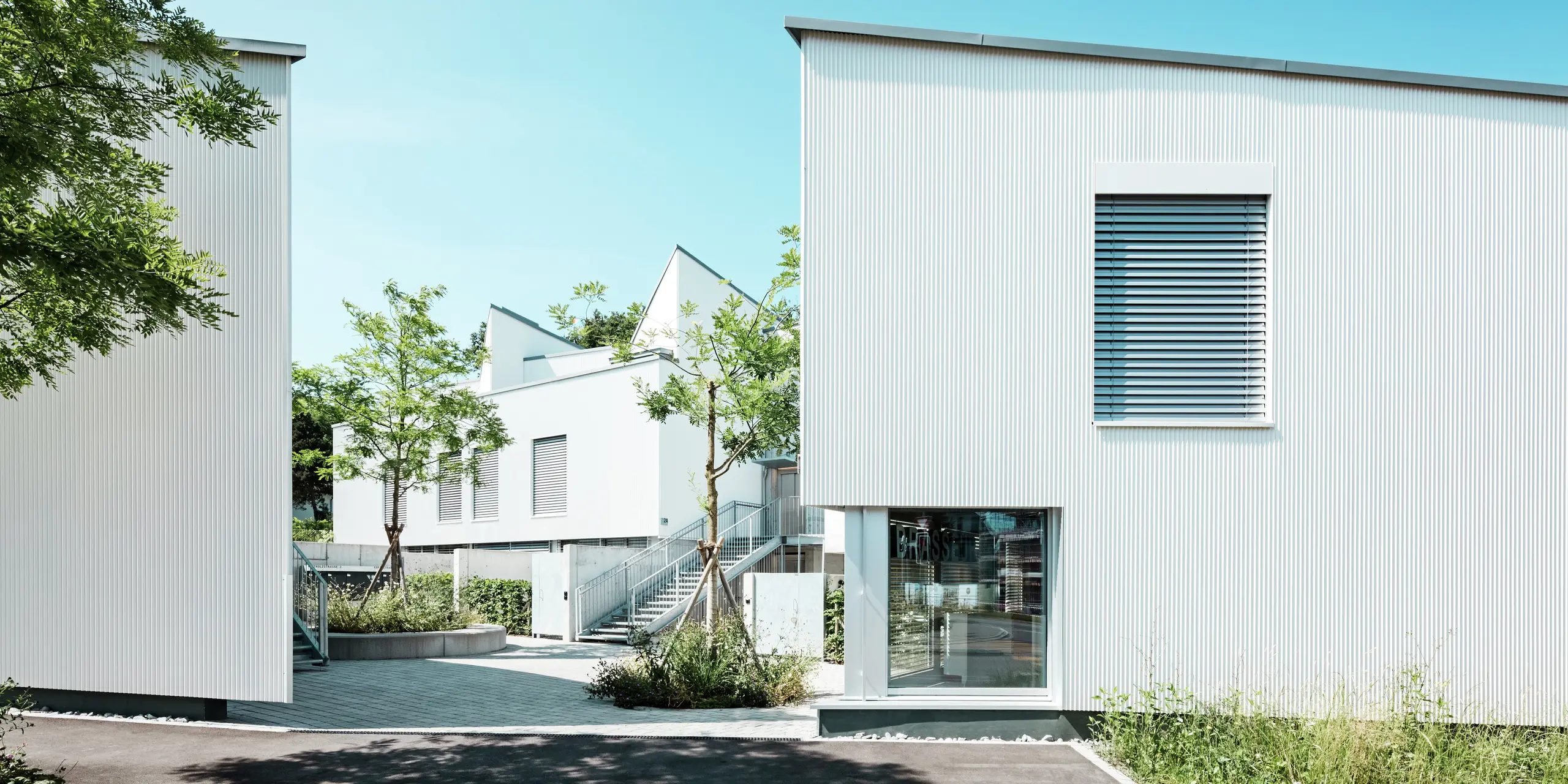 Une collection de mini-maisons modernes aux lignes épurées, revêtues du profil triangle PREFA P.10 blanc pur. La structure verticale de la façade en aluminium crée profondeur et légèreté, tandis que les stores vénitiens extérieurs allient fonctionnalité et esthétique. Le revêtement PREFA, résistant aux intempéries, offre durabilité et élégance intemporelle.