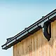 Angle de maison avec gouttière carrée PREFA en noir, avec caisson, fixation à l'aide de crochets de gouttière PREFA, façade revêtue de bois.