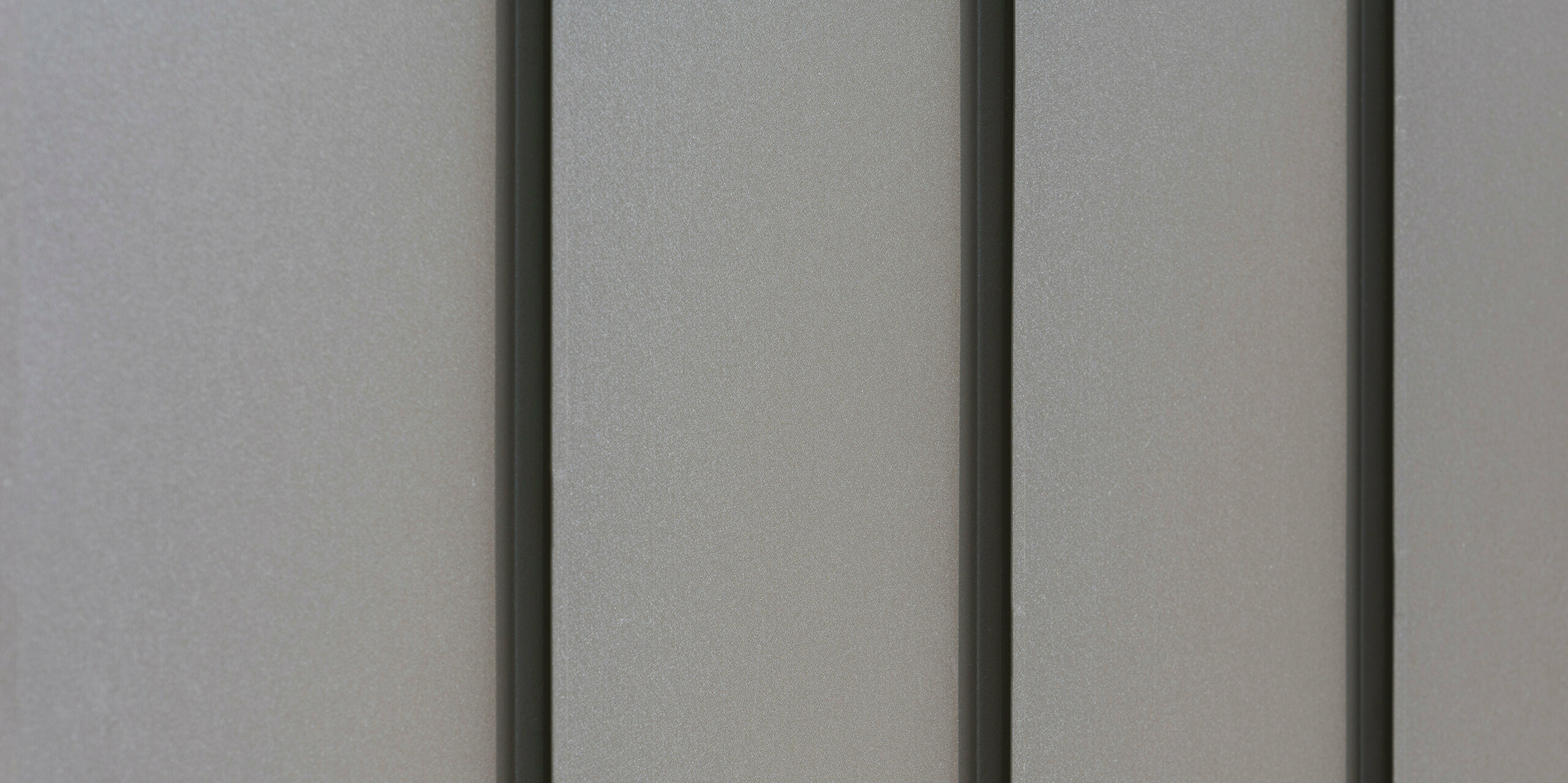 Gros plan d'un revêtement de façade moderne en aluminium avec des bacs verticaux créant un motif esthétiquement texturé. L'aluminium provient de PREFA Aluminium Products GmbH.