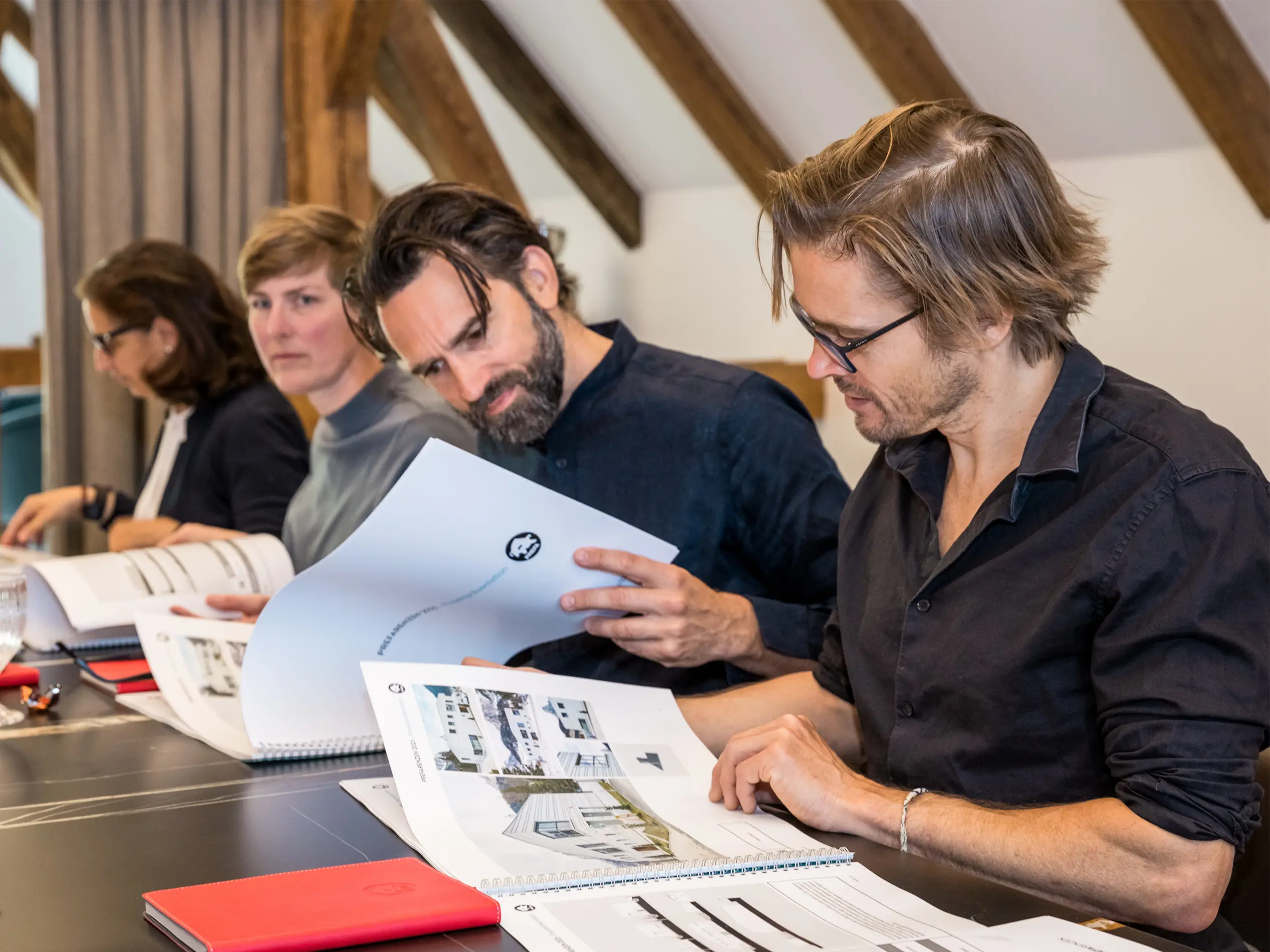Un jury d’architectes passe en revue les documents dans le cadre de la sélection des projets pour les PREFARENZEN 2025. Assis autour d’une table, les membres du jury analysent en détail les présentations de projets.
