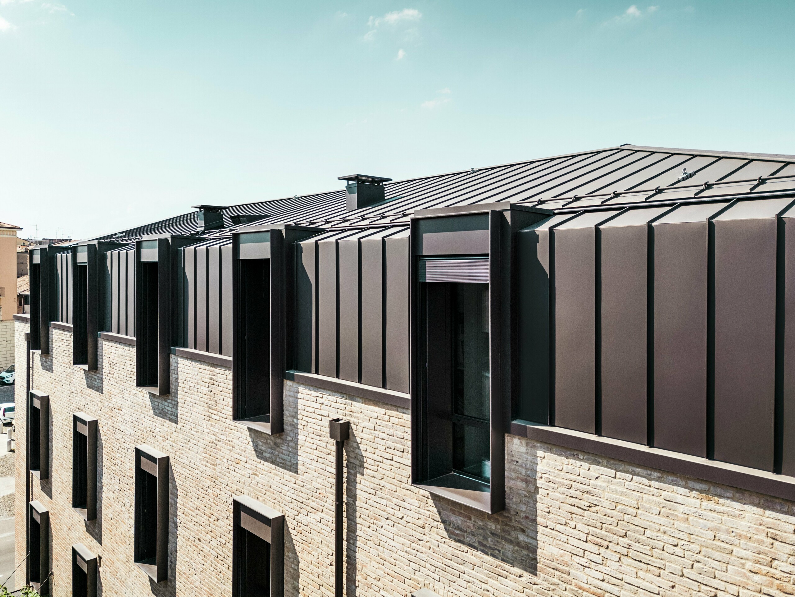 Conception moderne du toit et de la façade d'une maison en briques en Italie avec une toiture en aluminium PREFALZ de couleur P.10 brun noisette et des lucarnes caractéristiques.