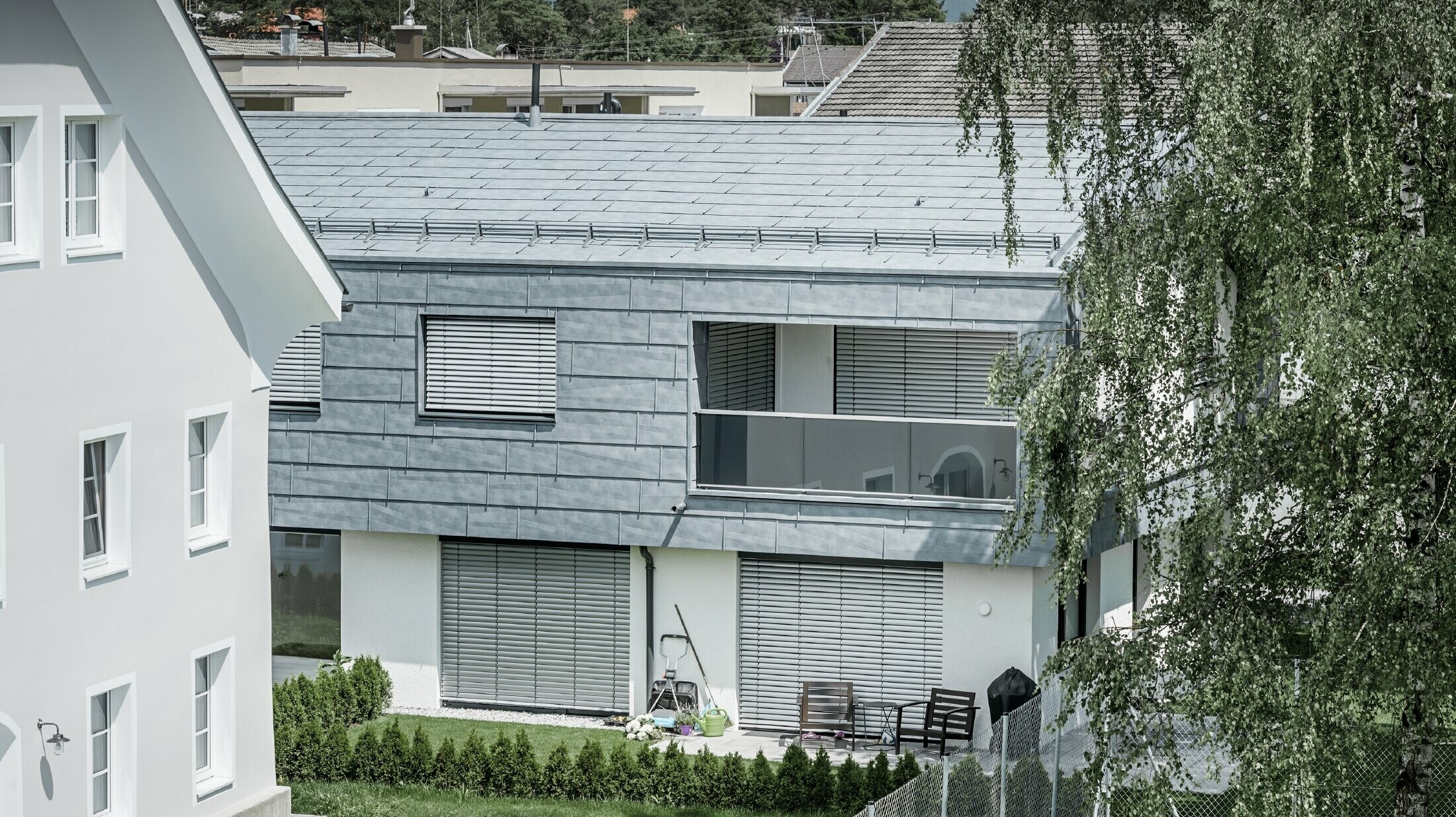 Maison individuelle classique avec toit à deux pans et deux lucarnes, recouverte de panneaux de toiture FX.12 PREFA couleur gris pierre.