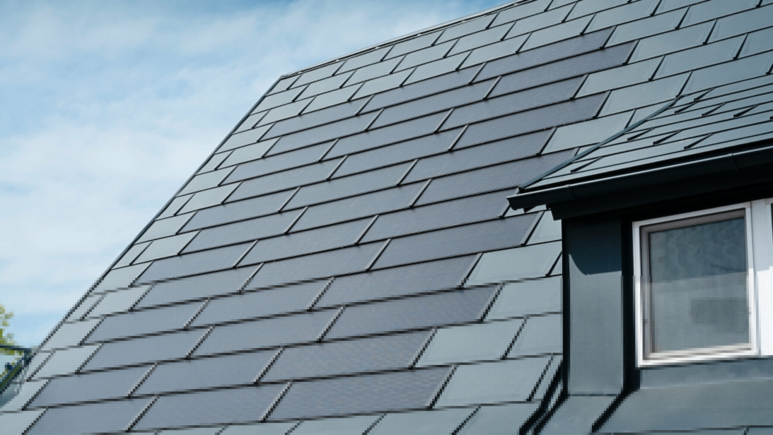 Vue détaillée du toit rénové d'une maison individuelle à Leonding avec des tuiles solaires PREFA de couleur anthracite. Le gros plan montre les panneaux en aluminium de haute qualité de PREFA, qui permettent une intégration transparente des modules solaires. Cette solution durable et résistante aux intempéries offre un moyen durable et économe en énergie de produire de l’électricité. L'image illustre la qualité esthétique et fonctionnelle des matériaux utilisés. Sur le bord droit de l’image, vous pouvez voir une fenêtre blanche sous une lucarne.