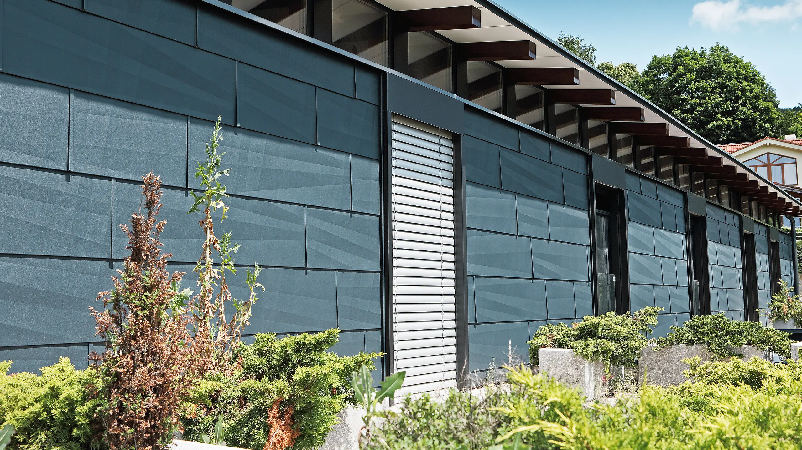 Côté exposé aux intempéries et donnant sur un jardin d’aspect moderne grâce au panneau de façade FX.12 couleur anthracite.