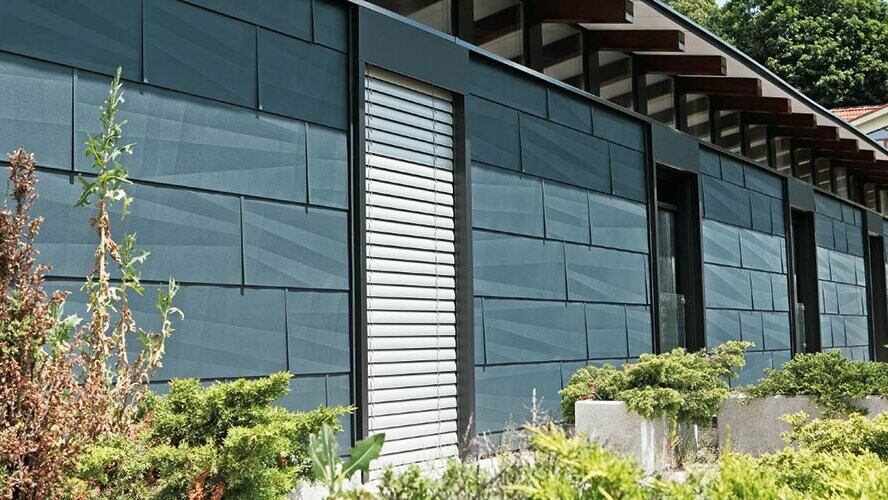 Côté exposé aux intempéries et donnant sur un jardin d’aspect moderne grâce au panneau de façade FX.12 couleur anthracite.