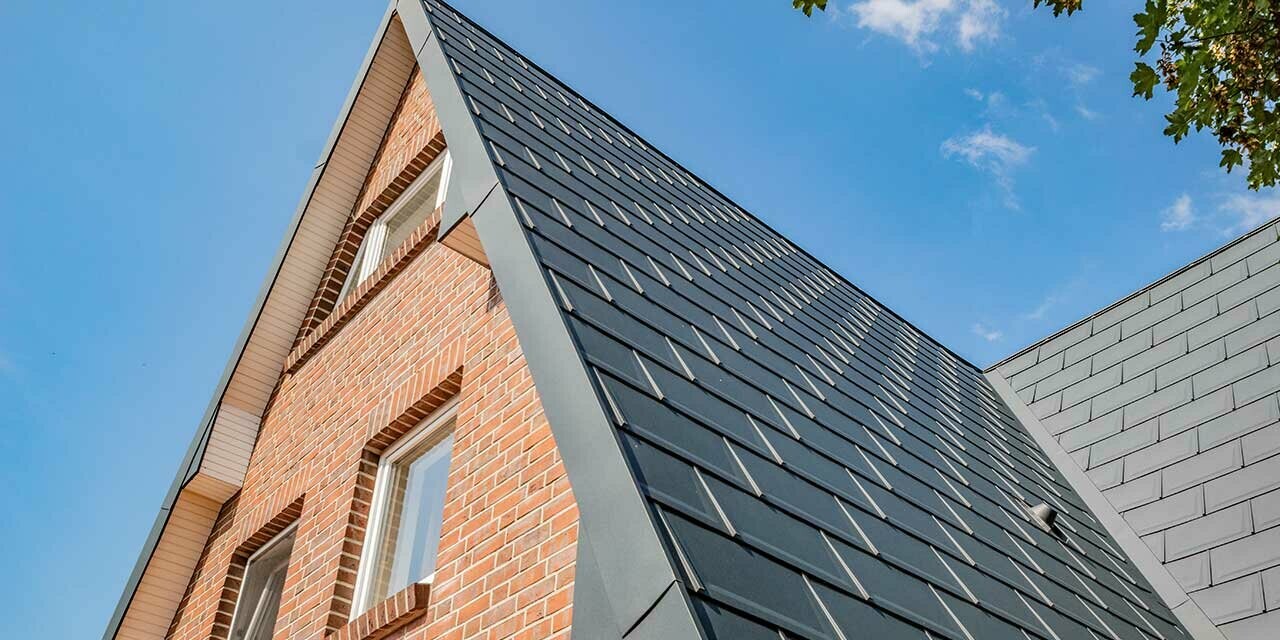 Toit à deux pans d’une maison à ossature en A, recouvert avec la tuile PREFA couleur anthracite et avec une façade en brique.