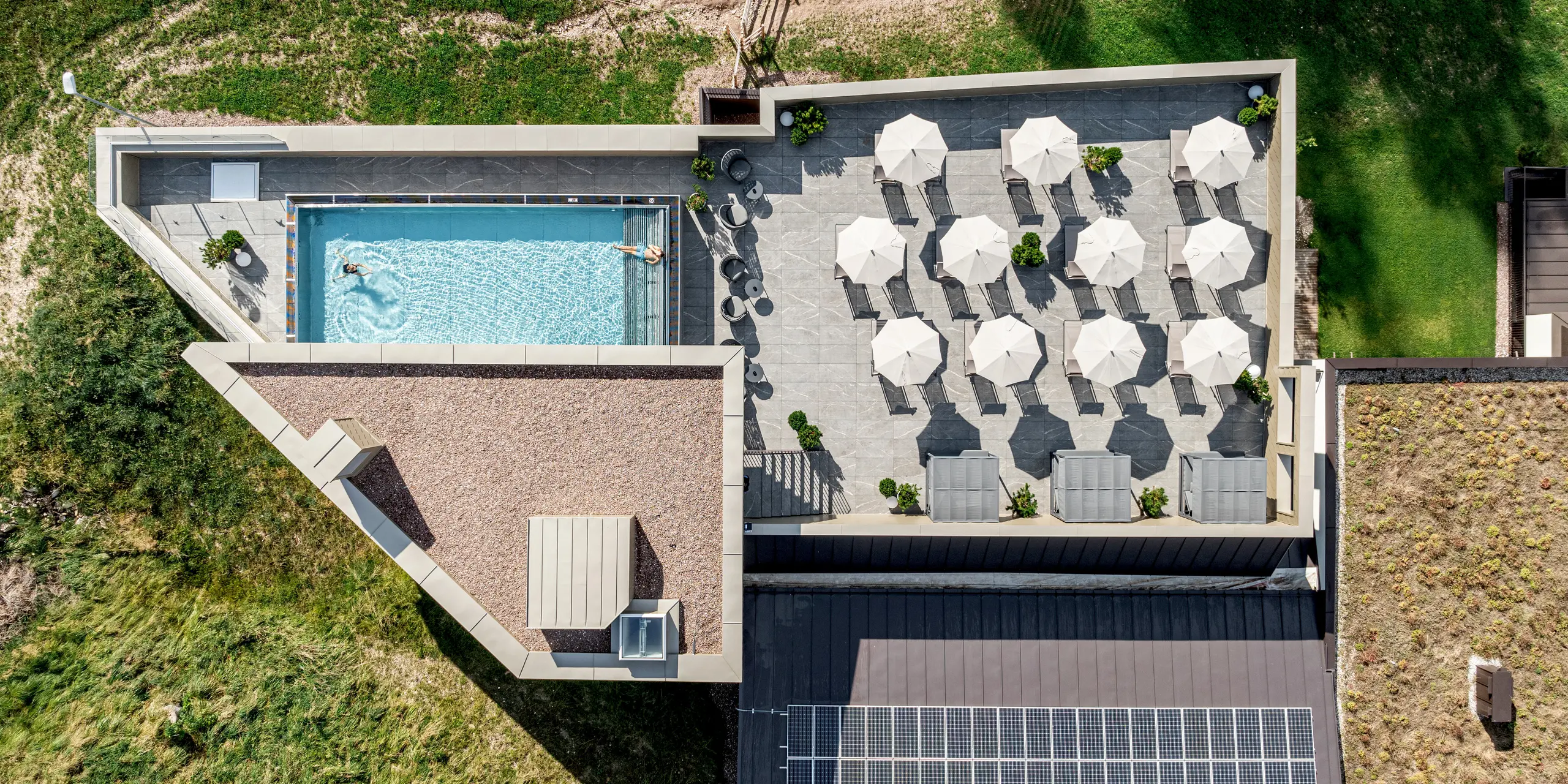 La vue aérienne révèle le Sporthotel Obereggen, un établissement moderne du Tyrol du Sud, avec sa vaste terrasse ensoleillée et sa piscine extérieure. La façade en aluminium PREFA et le parapet en bronze créent un contraste saisissant avec le paysage alpin verdoyant. Durables, résistants aux intempéries et nécessitant peu d'entretien, les produits en aluminium PREFA séduisent par leur élégance, leur grande stabilité et leur qualité pérenne – un choix idéal pour une architecture raffinée en milieu alpin.