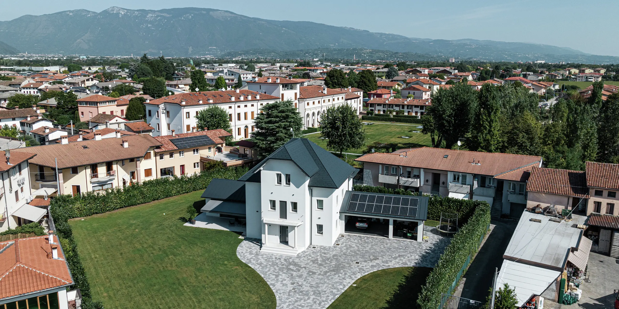 Vue aérienne d'une maison familiale moderne à Marano Vicentino, en Italie, avec un toit robuste en bardeaux PREFA en P.10 anthracite. Les dépendances adjacentes sont équipées d'une toiture classique à joint debout en aluminium. La toiture en aluminium de haute qualité garantit une conception de toit durable et esthétique.