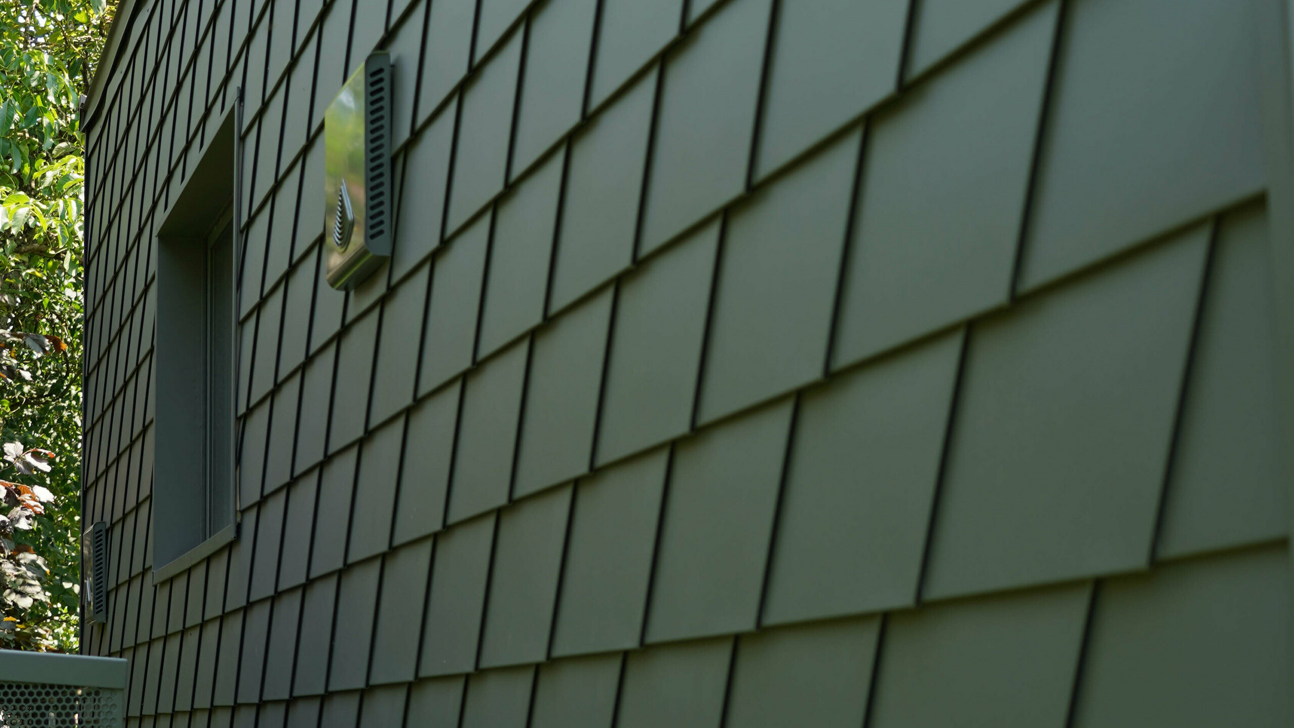 Prise de vue centrée sur l'arrière du bureau mobile où toute la façade est revêtue de bardeau en aluminium PREFA 
