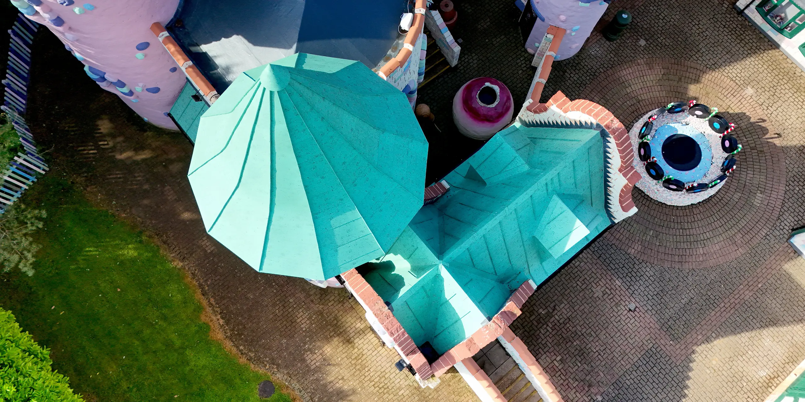 Vue aérienne dynamique du complexe féerique du château de Sundown Adventureland, mettant en valeur ses tours coniques imposantes et ses toitures aux multiples facettes. Les toitures en aluminium PREFALZ, couleur P.10 vert de gris, attirent immédiatement le regard et soulignent l'architecture ludique grâce à leurs joints debout précis et leurs lignes épurées. La grande malléabilité du matériau permet des solutions parfaites pour les géométries complexes, tandis que sa surface robuste et résistante à la corrosion garantit une qualité durable et une protection fiable par tous les temps.