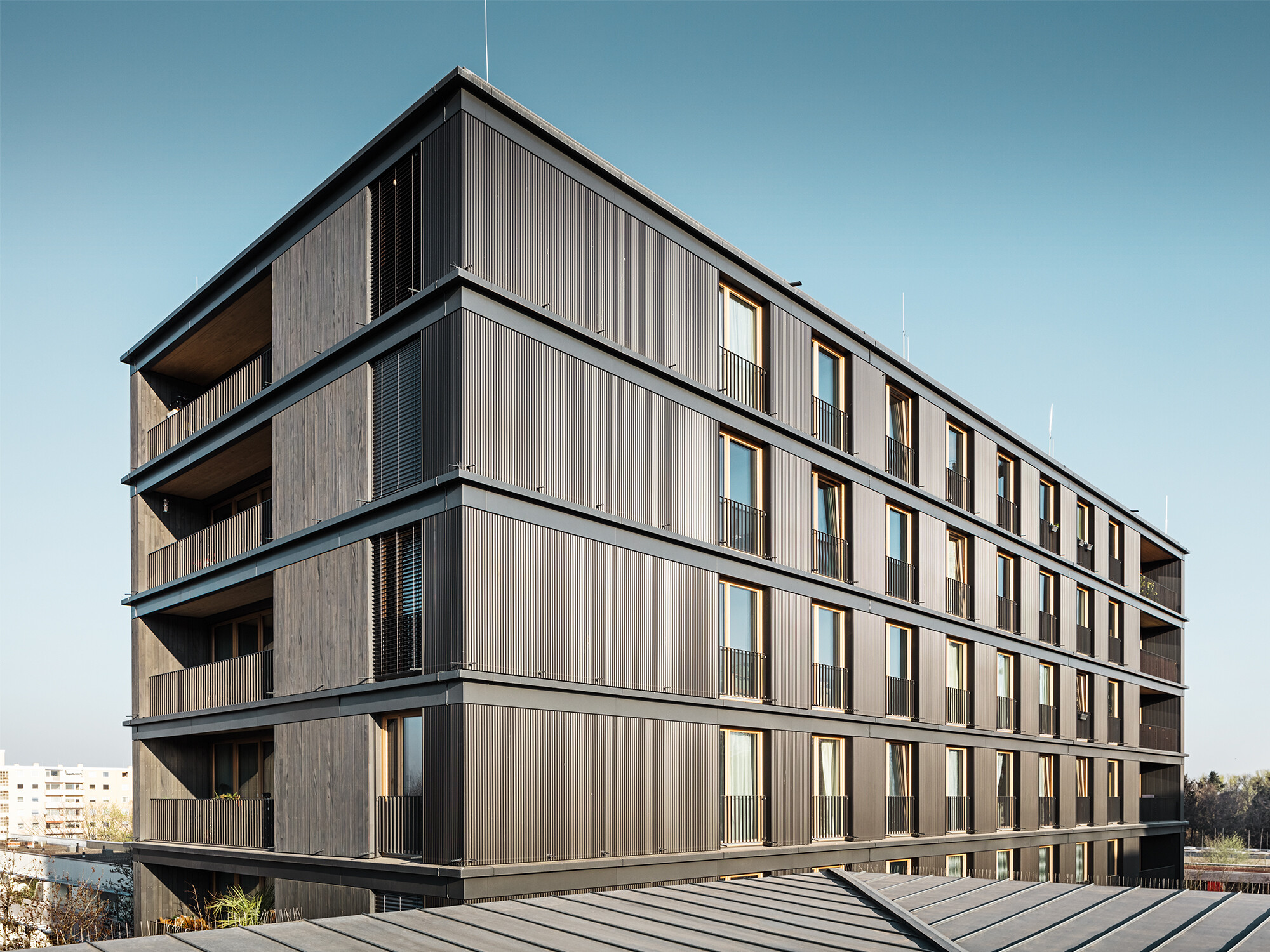 L'immeuble d'habitation et de bureaux vu de côté : le profil ondulé de PREFA et la façade en bois sont presque indiscernables.
