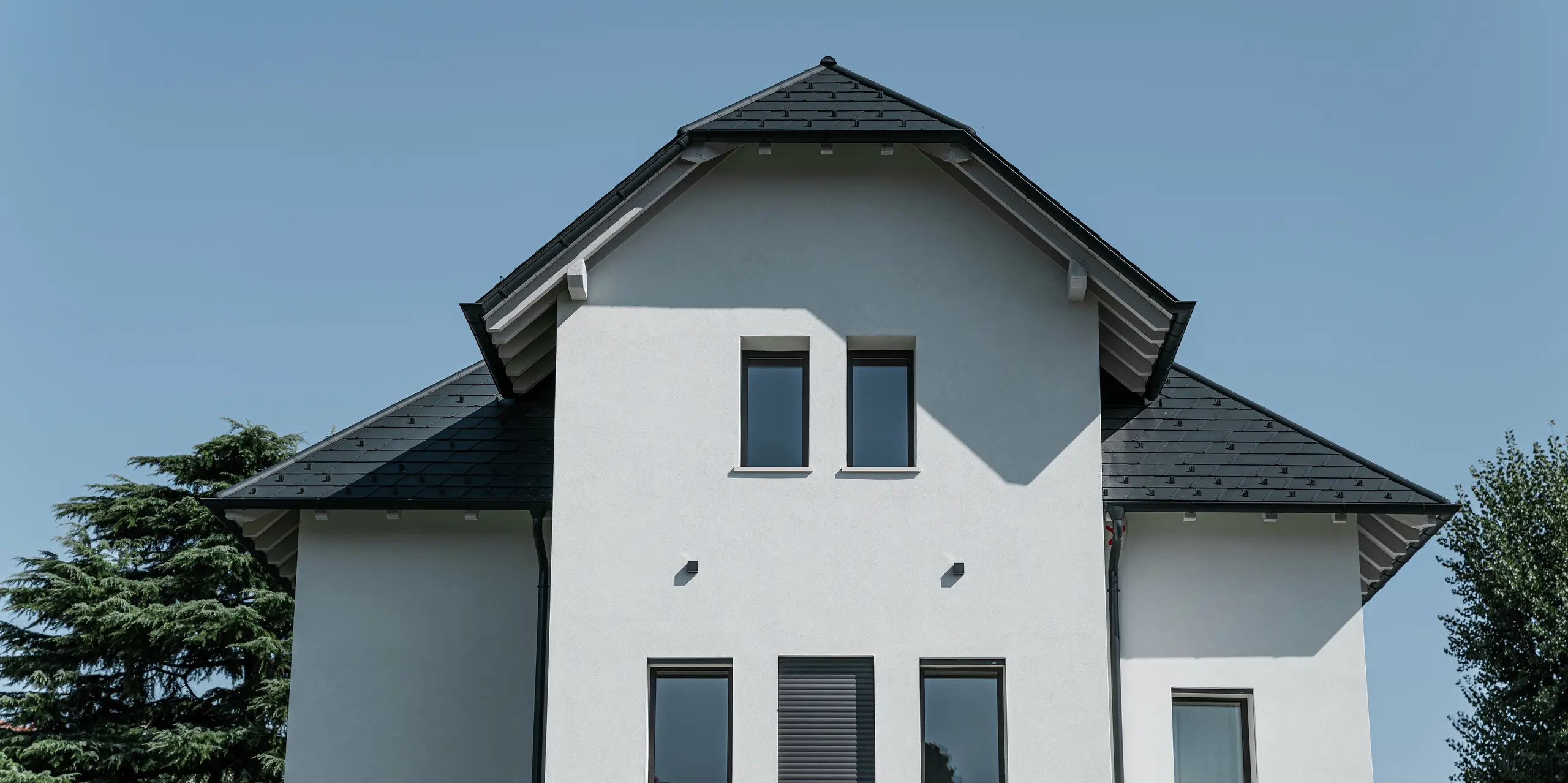 Gros plan du pignon d'une maison unifamiliale moderne à Marano Vicentino, en Italie, avec un toit PREFA en bardeaux de couleur P.10 anthracite. La forme frappante du toit et les produits en aluminium de haute qualité garantissent une solution de toit élégante et durable sur le bâtiment de trois étages.