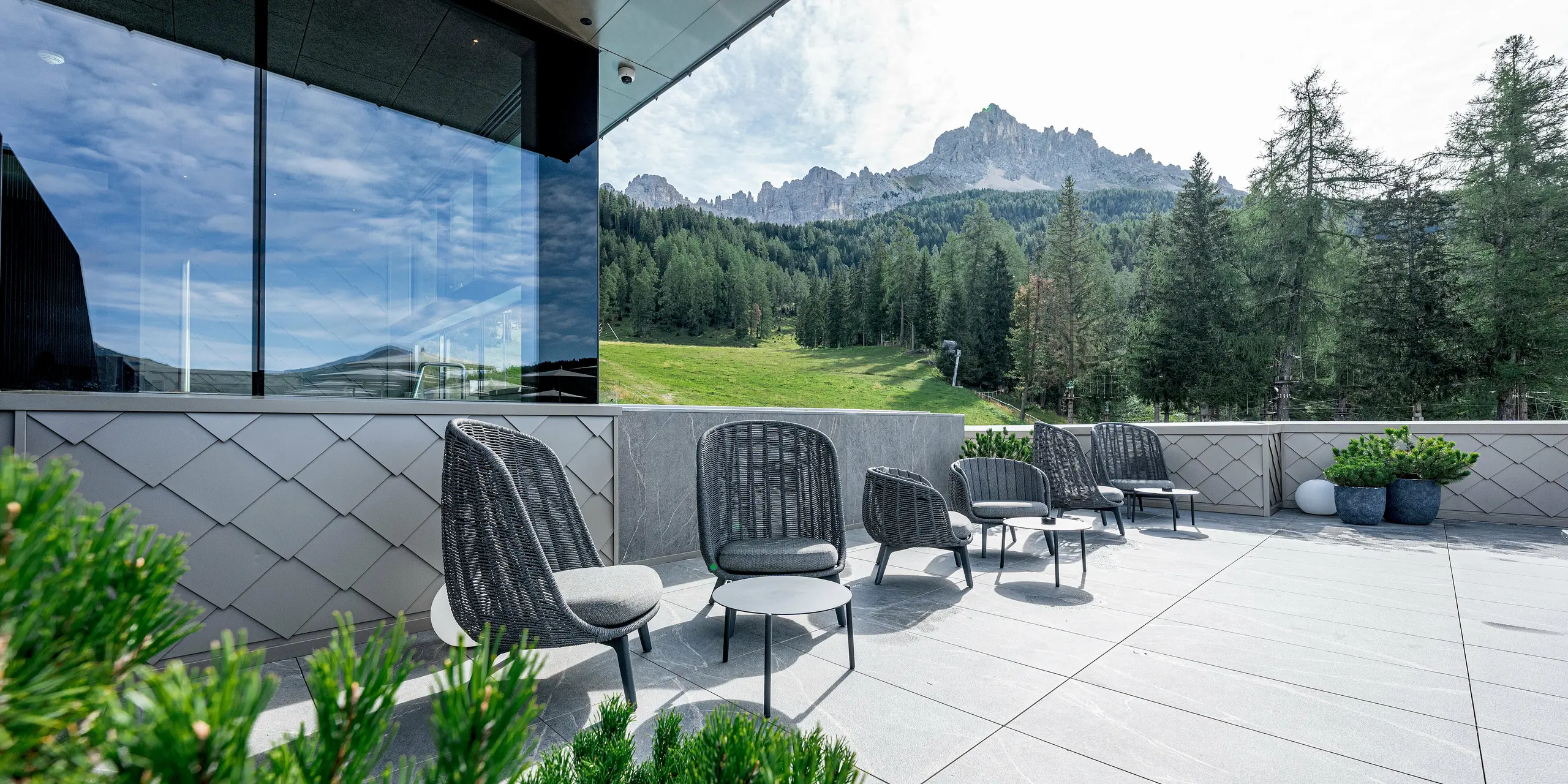 La terrasse du Sporthotel Obereggen, au Tyrol du Sud, est aménagée avec des sièges modernes et de grandes dalles de pierre, offrant une vue imprenable sur le panorama alpin. La façade en aluminium PREFA, avec son motif de losanges de façade 29x29 couleur bronze, apporte une touche architecturale élégante. La structure finement dessinée en losanges révèle un aspect à la fois dynamique et sophistiqué selon l'angle de la lumière. Grâce à leur durabilité, leur résistance aux intempéries et leur absence d'entretien, les produits en aluminium PREFA sont parfaitement adaptés aux terrasses d'hôtels exposées en régions alpines.