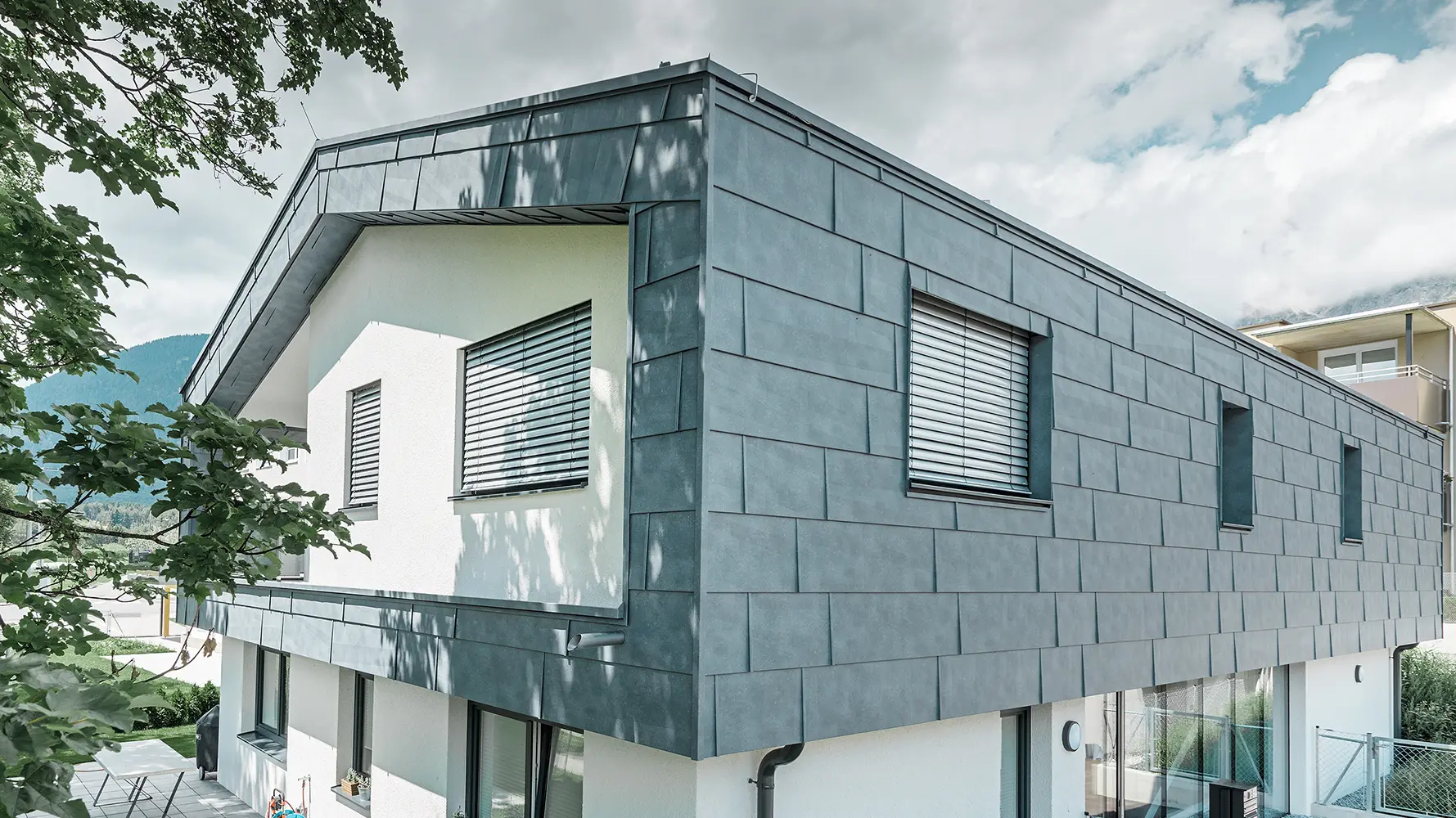 Maison individuelle moderne sans avancée de toit. L’étage supérieur a été recouvert de panneaux de façade FX.12 PREFA couleur gris pierre et le reste de la façade a été crépi en blanc.