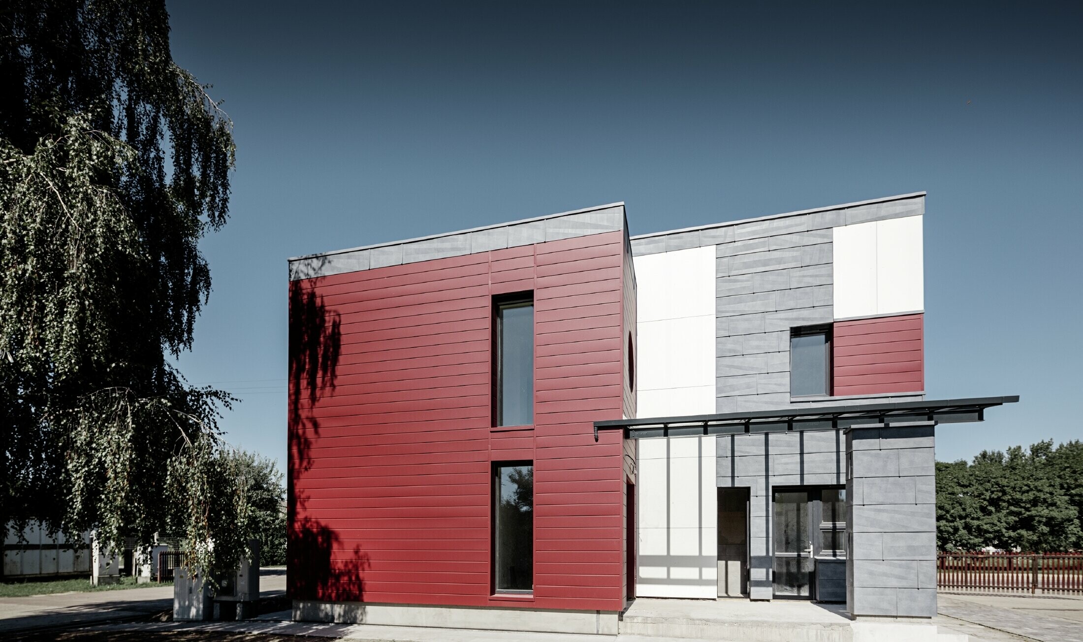 Complexe de bureaux moderne — Façade tricolore (blanc, rouge et gris pierre) réalisée à partir de produits en aluminium PREFA (sidings, panneaux de façade FX.12 et panneaux composites en aluminium)