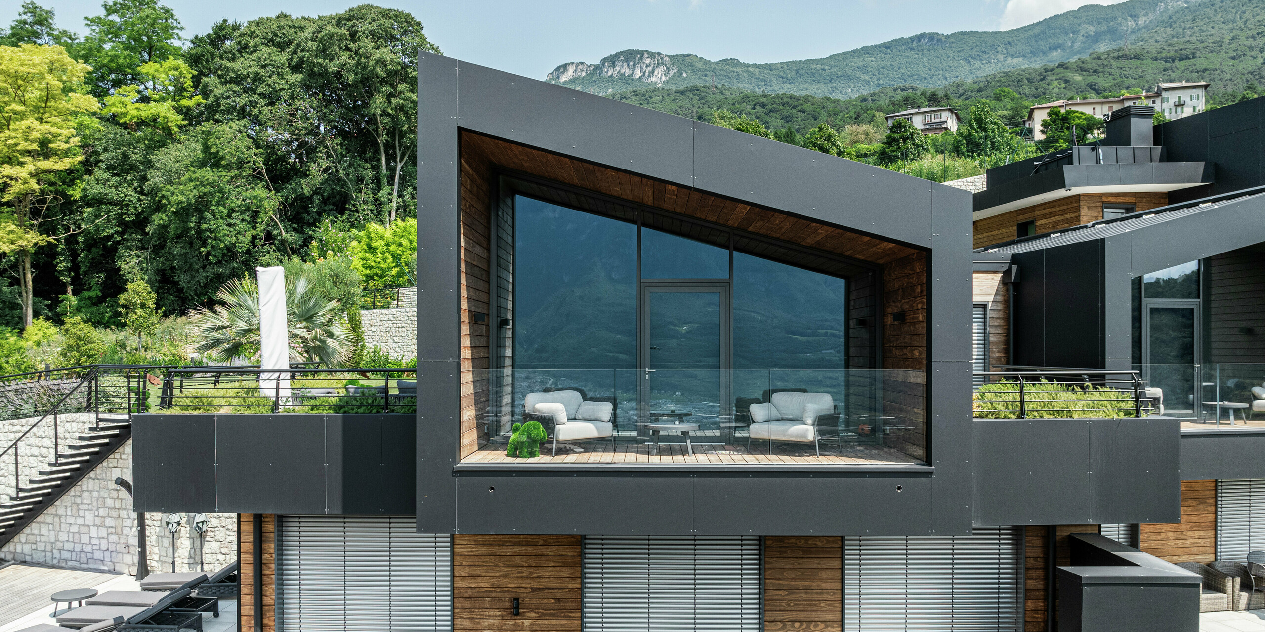 Bâtiment résidentiel moderne avec un toit en pente distinctif et de grandes fenêtres, offrant des vues spectaculaires sur le paysage montagneux de Trente. La façade en panneaux composites en aluminium PREFA en noir P.10 offre un aspect élégant et résistant aux intempéries, tandis que le bois chaud crée un contraste harmonieux. La loggia couverte avec garde-corps en verre relie l'intérieur et l'extérieur et offre le plus haut niveau de confort de vie. Les matériaux durables et les produits PREFA durables garantissent protection, stabilité et esthétique intemporelle.