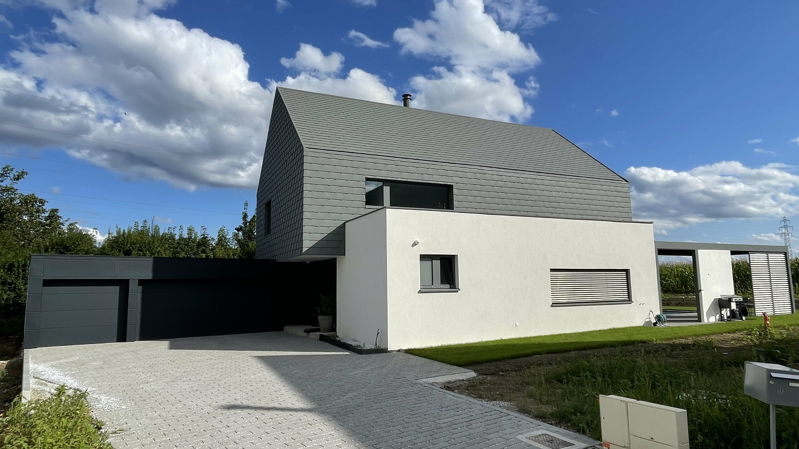 Vue éloignée de l'avant de cette maison moderne alsacienne. On aperçoit la cours pavée, le garage et les éléments en aluminium PREFA.